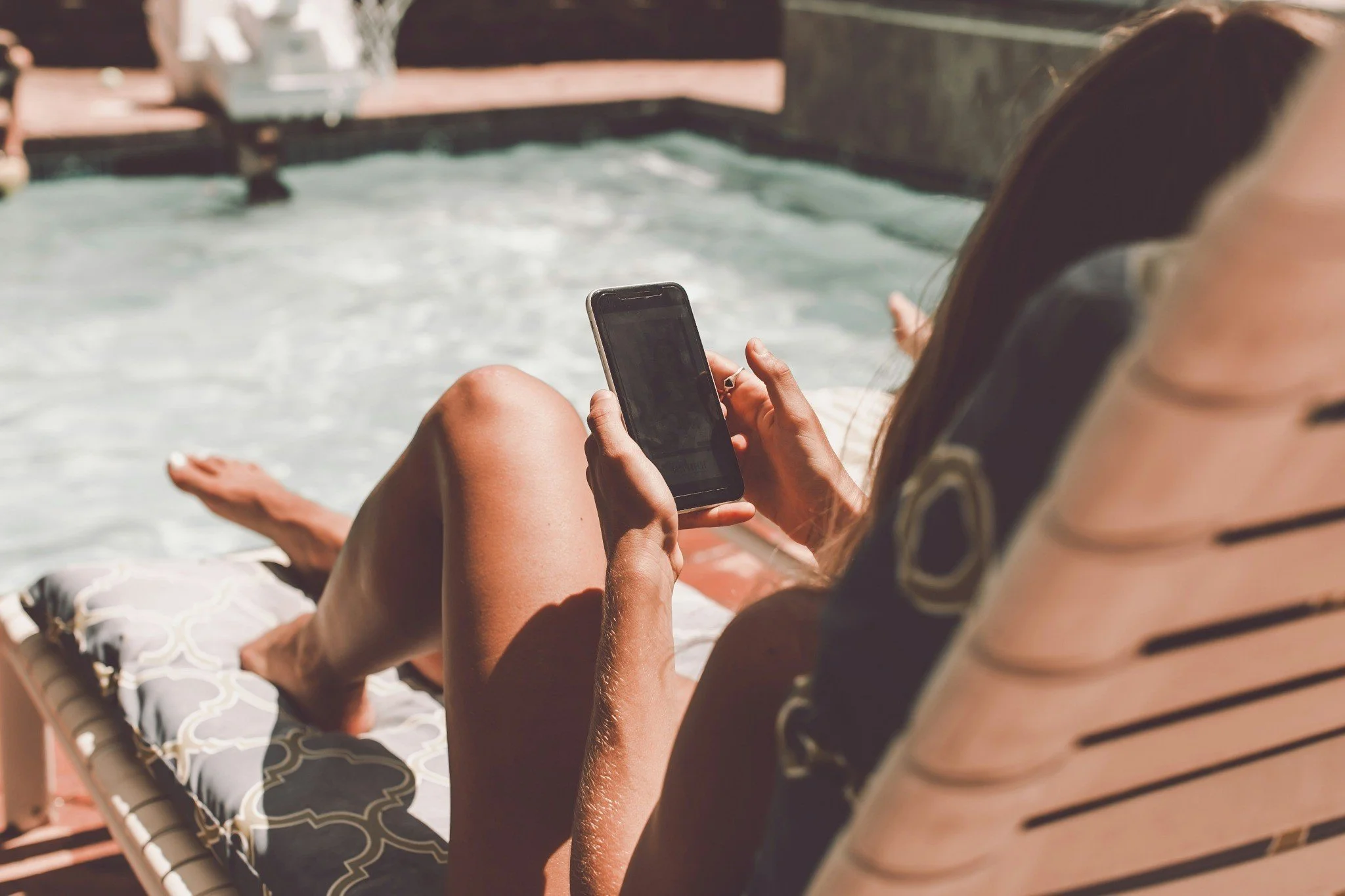 Woman relaxing by a pool while scrolling social media, symbolizing comparison and modern expectations of lifestyle.