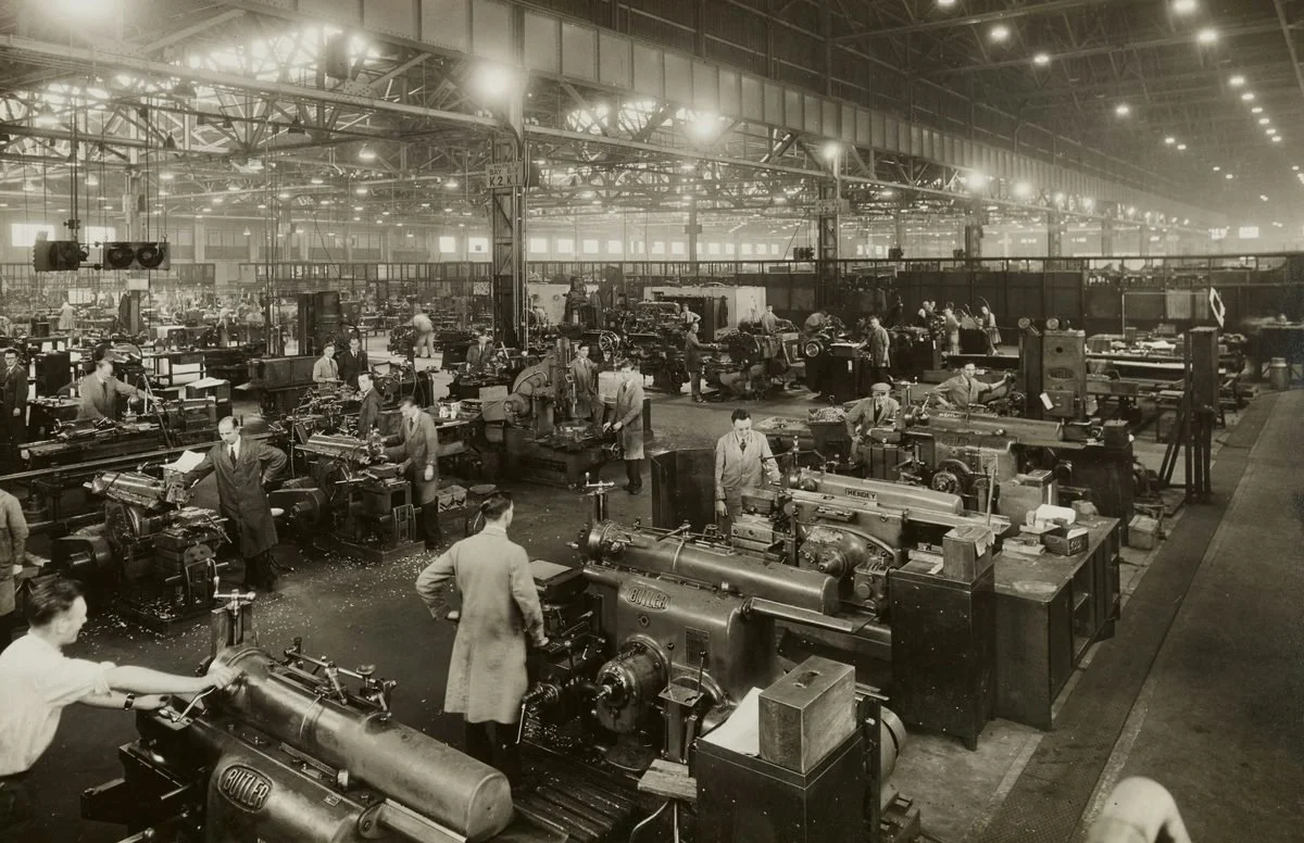 Black and white photo of industrial factory workers at machines — history of overwork culture.