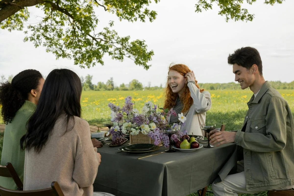Friends laughing together at outdoor table — social connection doesn't require high spending, stealth wealth and frugality.