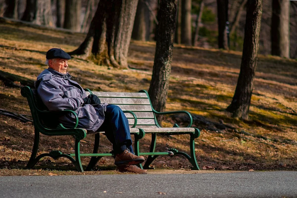 Older man sitting alone on park bench in autumn — reflecting on life, work, and regrets.