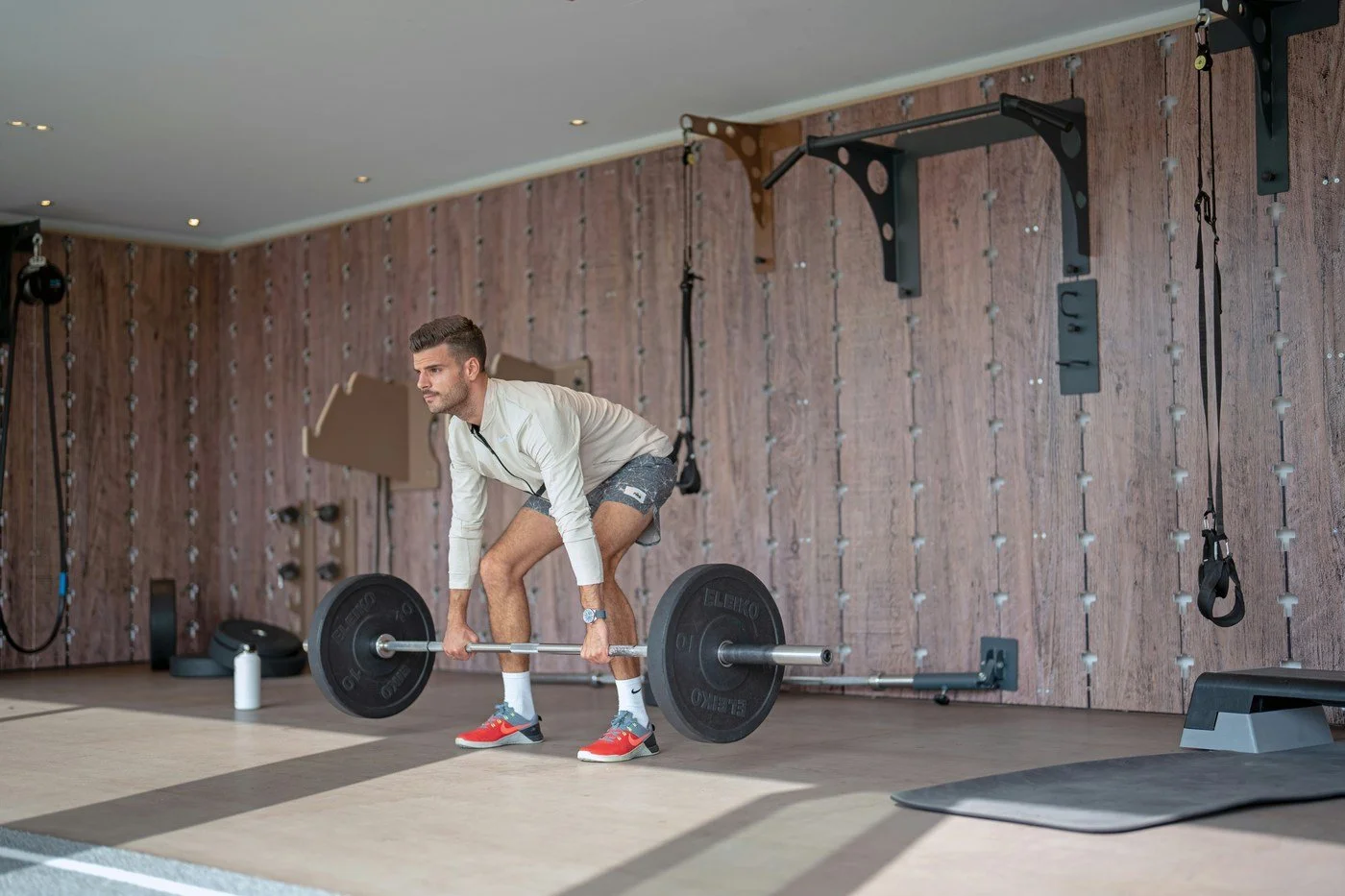 Man performing a barbell deadlift in a home gym setting, representing strength training as a key lever for biological age and longevity.
