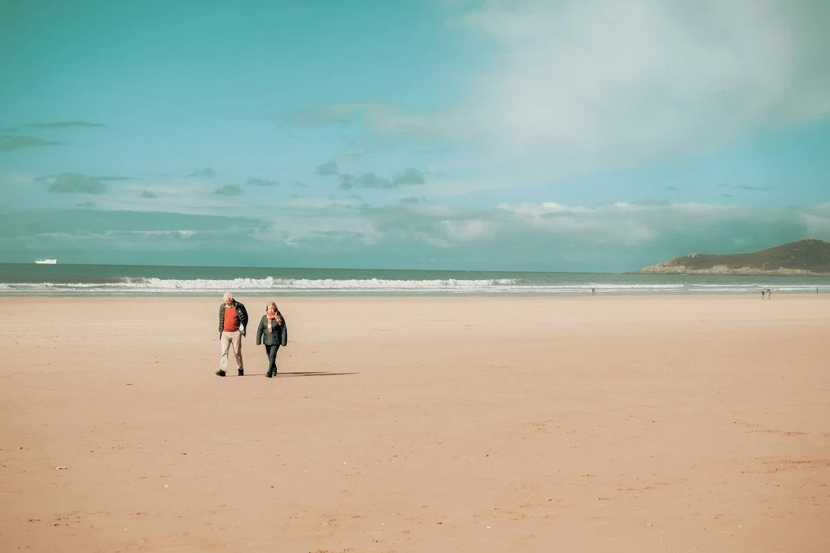Elderly couple walking together on a beach — maintaining an active routine in retirement is the compound return of decades of healthy choices.
