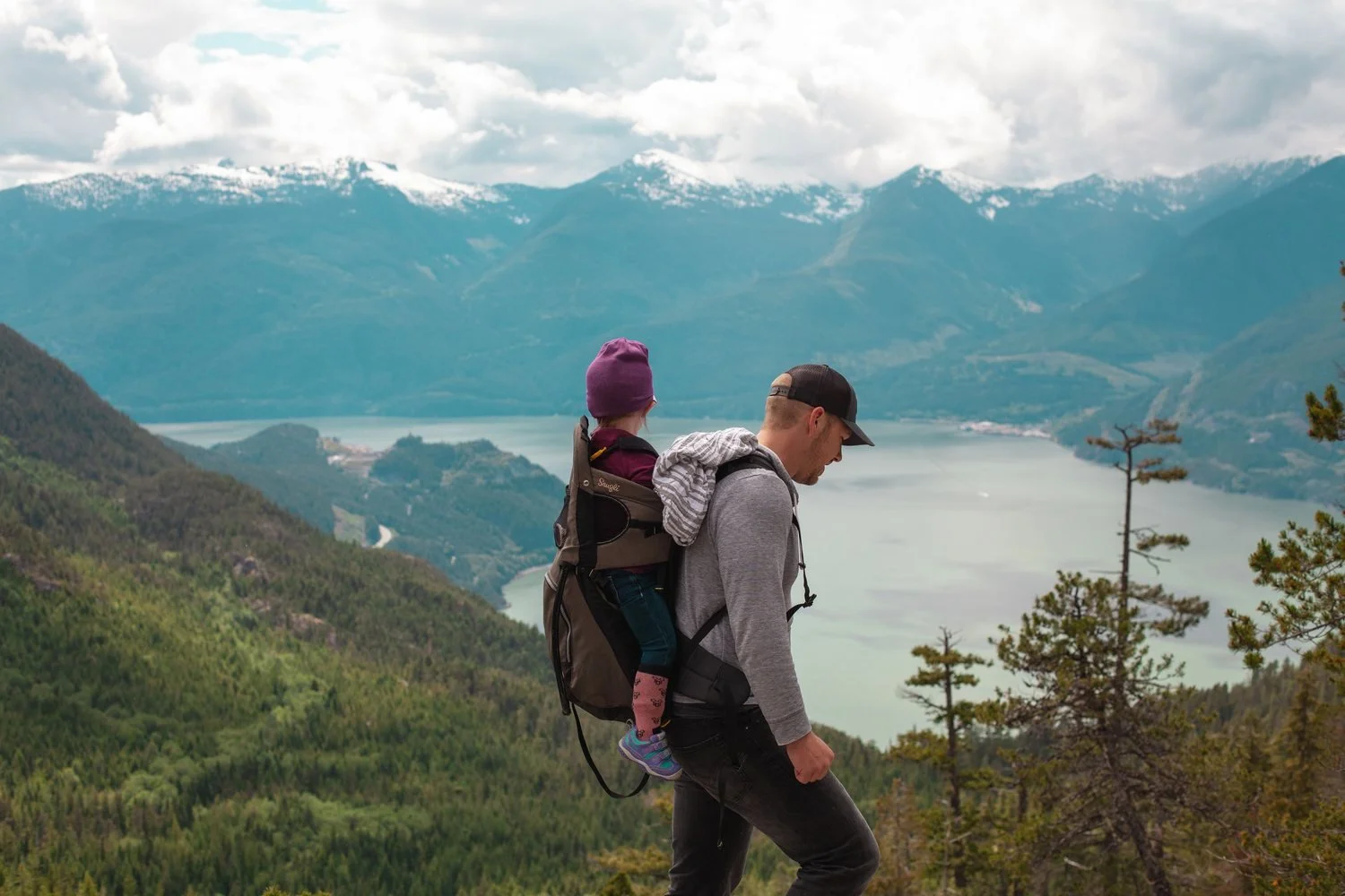 A father hiking through mountains with his young child in a backpack carrier, representing money as a tool for freedom and time together rather than accumulation.