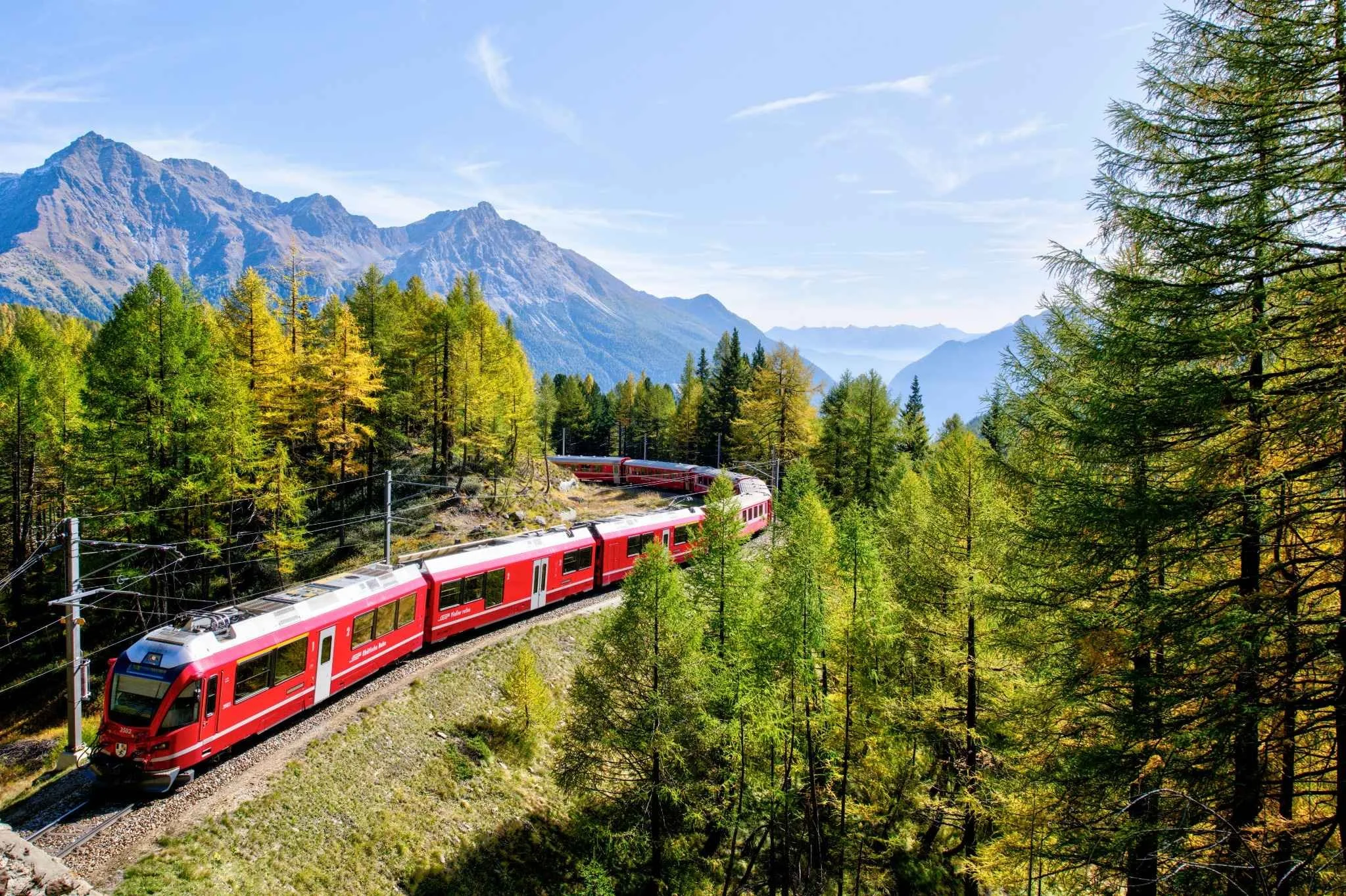 Red electric train traveling through mountains public transport low carbon mobility.