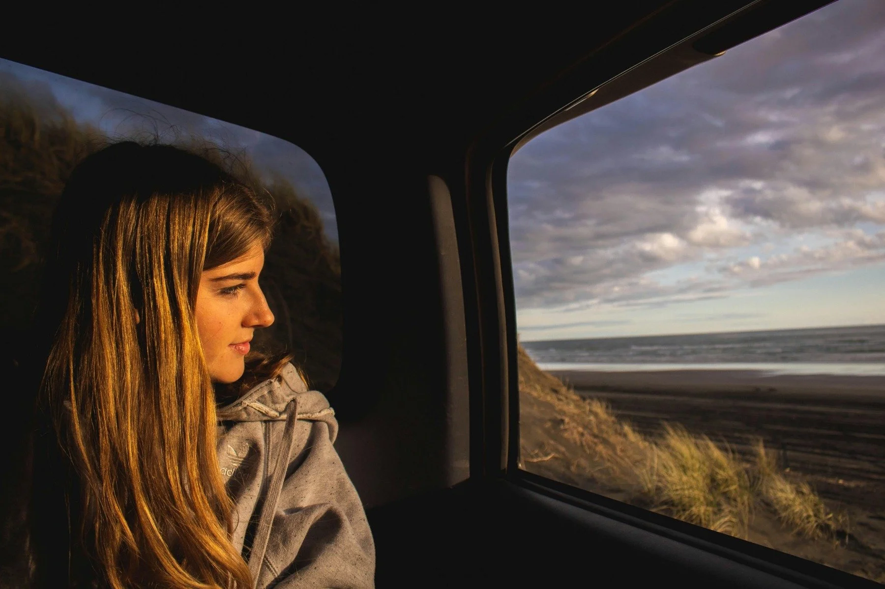 Young woman looking out a car window toward the ocean, reflecting on her future self and long-term saving goals.