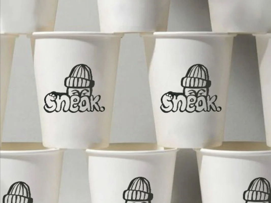 Multiple white cups with a black logo of a beanie-wearing character and the word 'sneak' on them, stacked in rows.