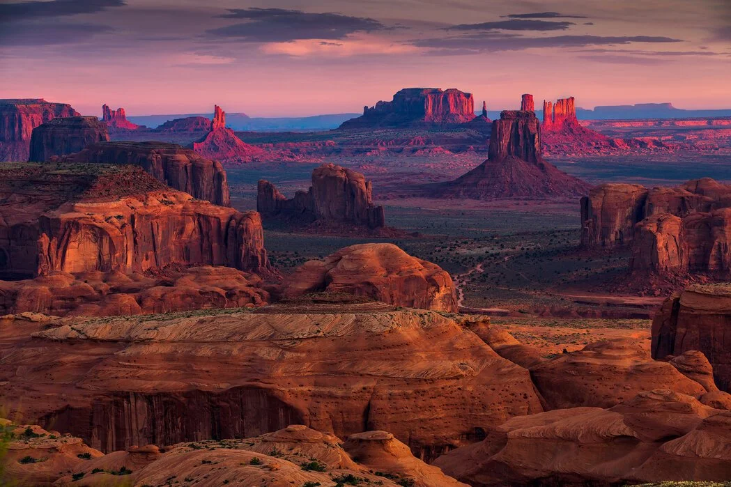 Scenic view of Monument Valley at sunset, featuring red sandstone mesas and buttes under a colorful sky.
