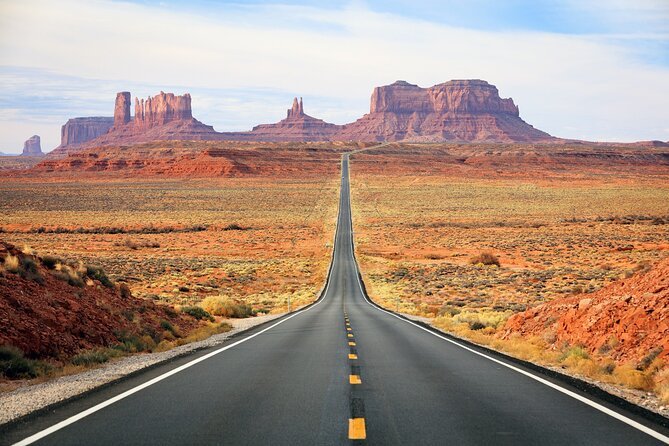 A long straight road through a desert landscape with red rock formations in the background.
