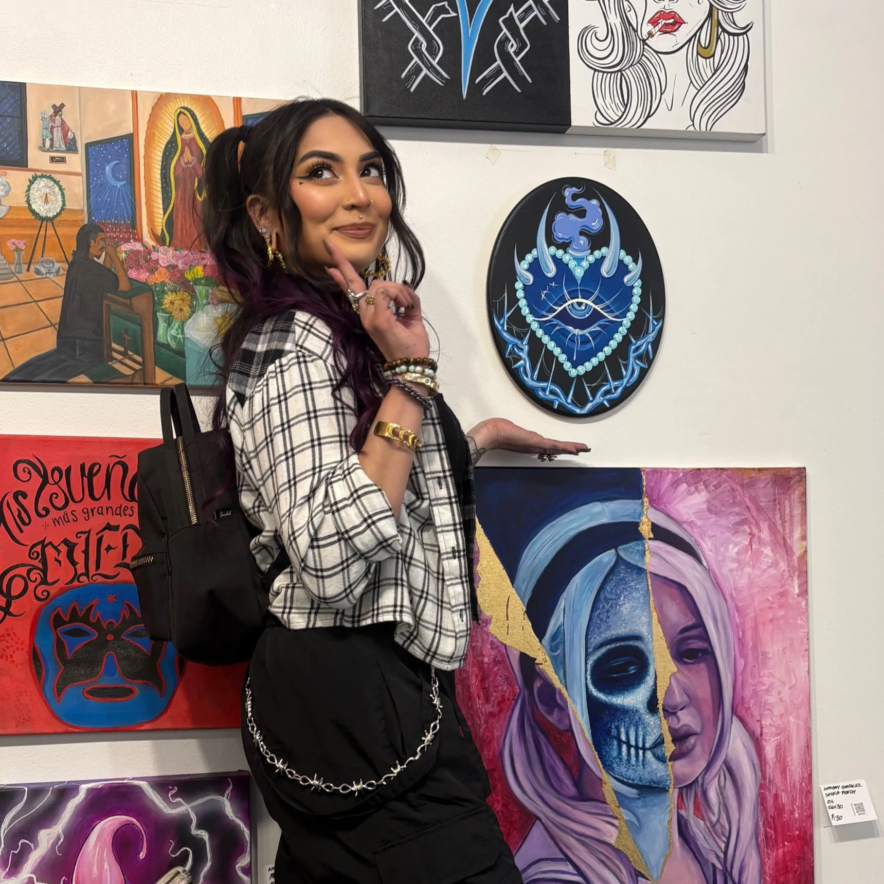 A woman with dark hair and purple highlights posing in front of colorful artwork at an art gallery.