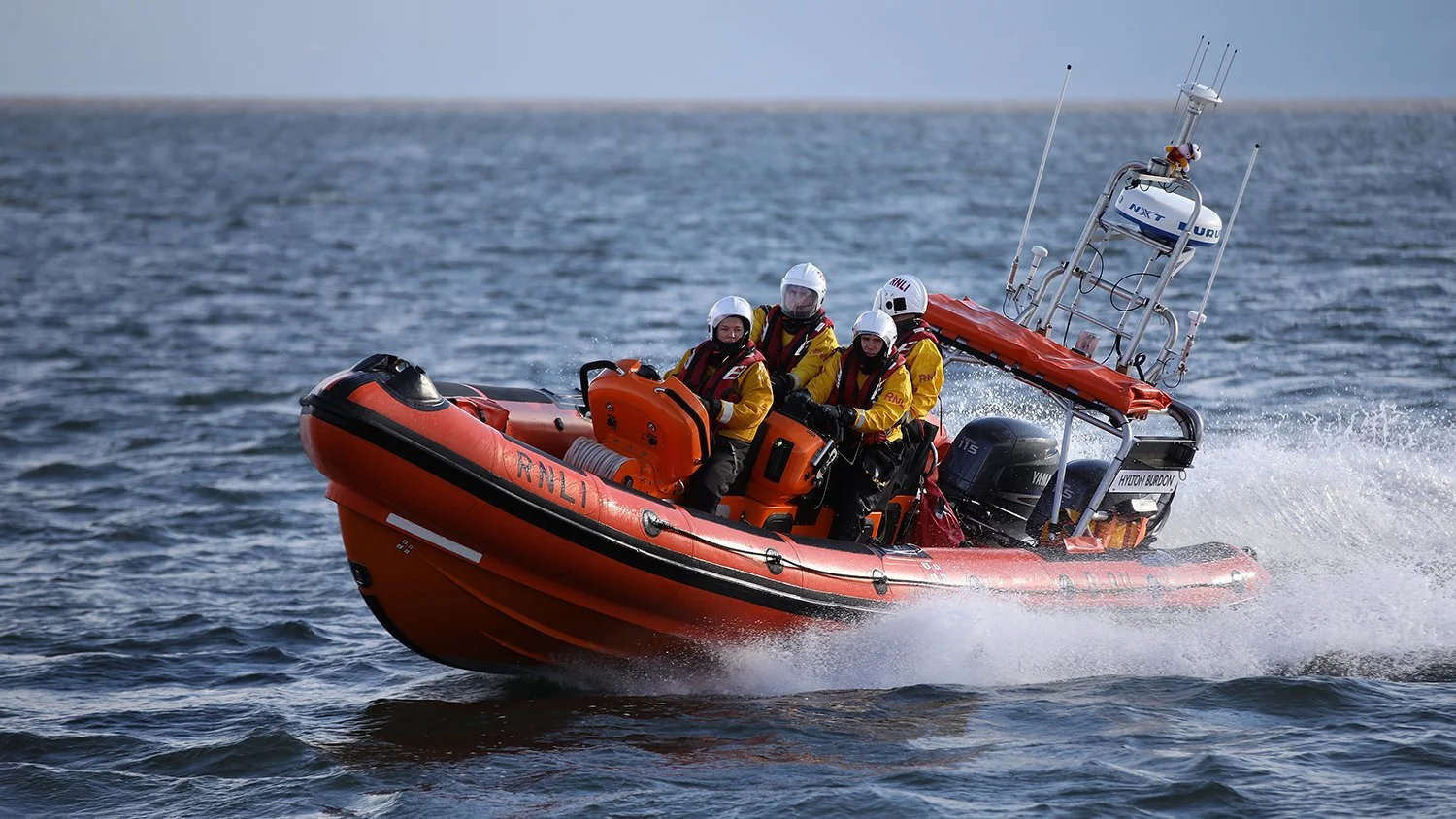 A rescue boat with five crew members in yellow jackets and helmets speeding through the water.