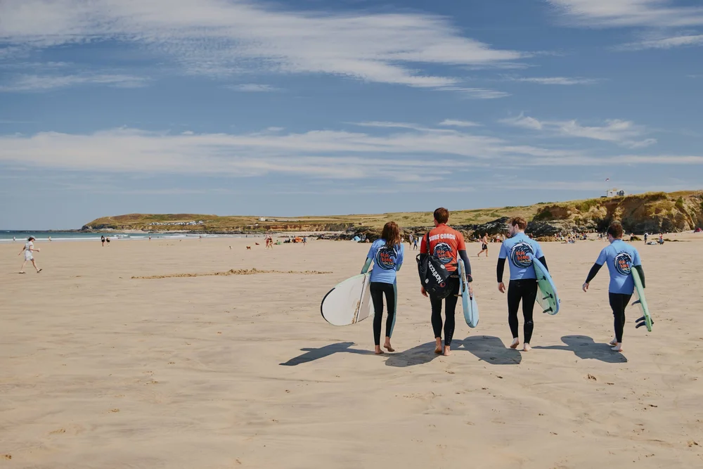 Private surf lesson walking down a Cornish beach with surfboards