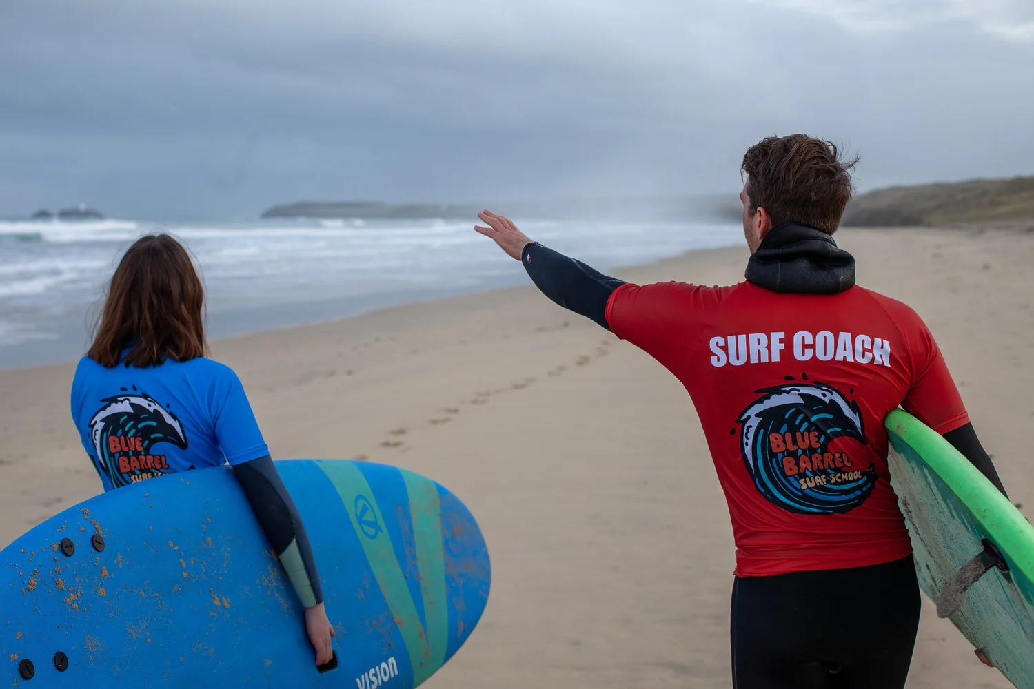 Blue Barrel surf coach pointing out the waves to a surfer on a Cornish beach