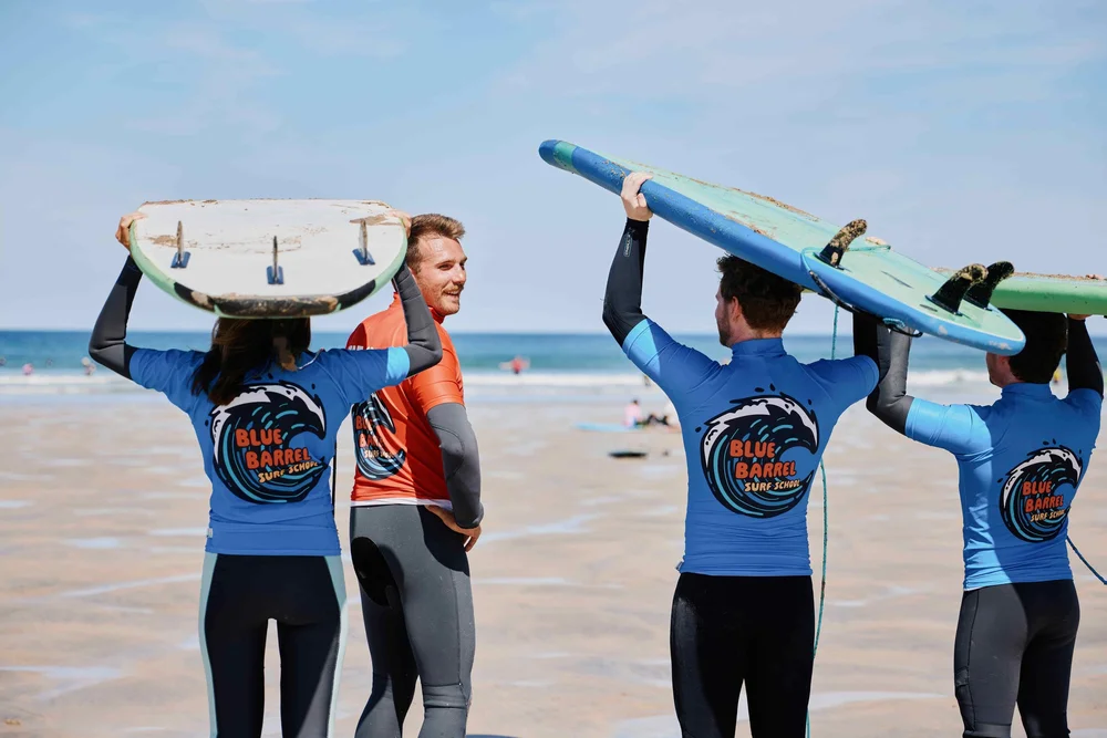 Friends laughing and carrying surfboards on their heads on a group surf lesson in Cornwall