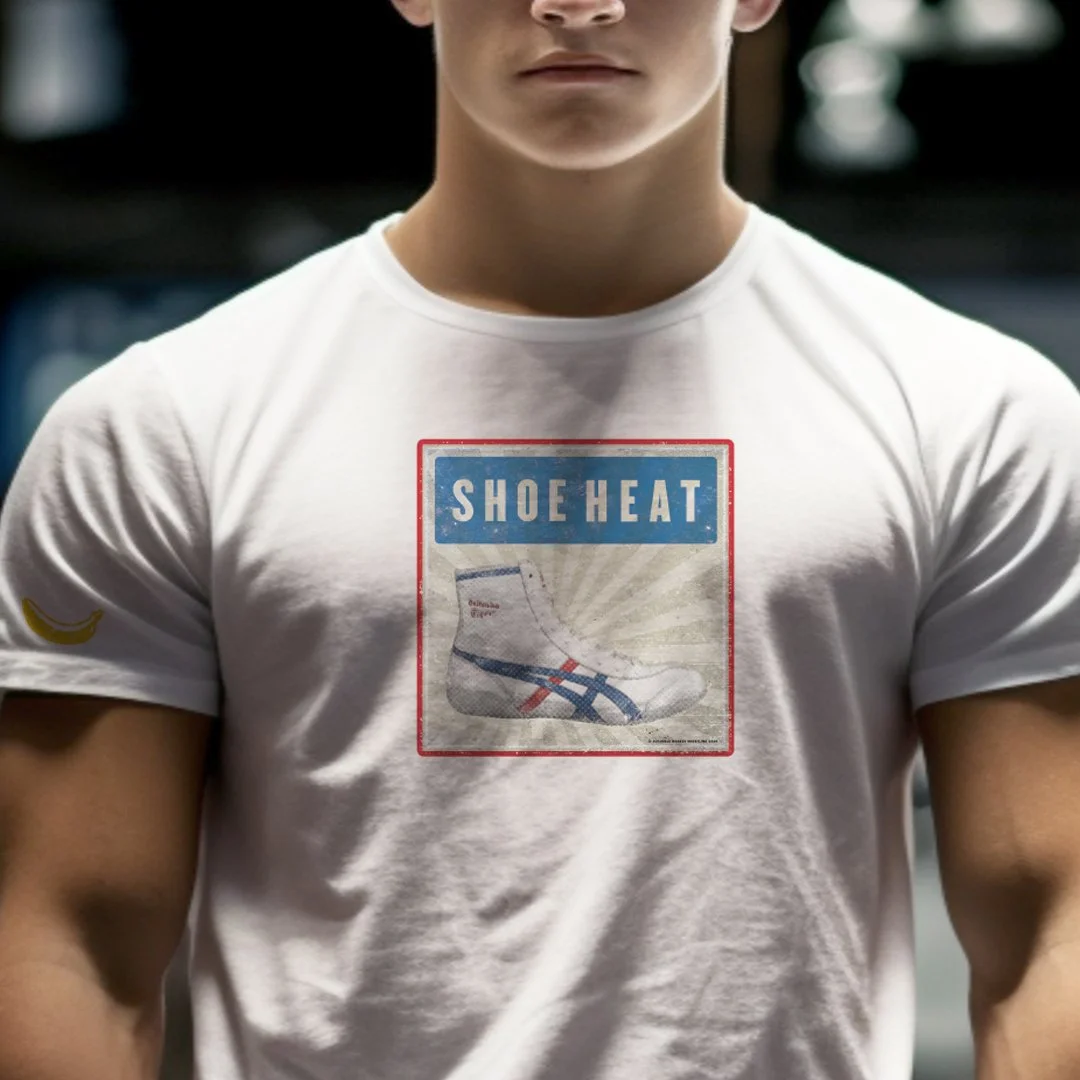 Person wearing a white t-shirt with a vintage-style graphic featuring a shoe and the text 'Shoe Heat' on the chest area, indoors.