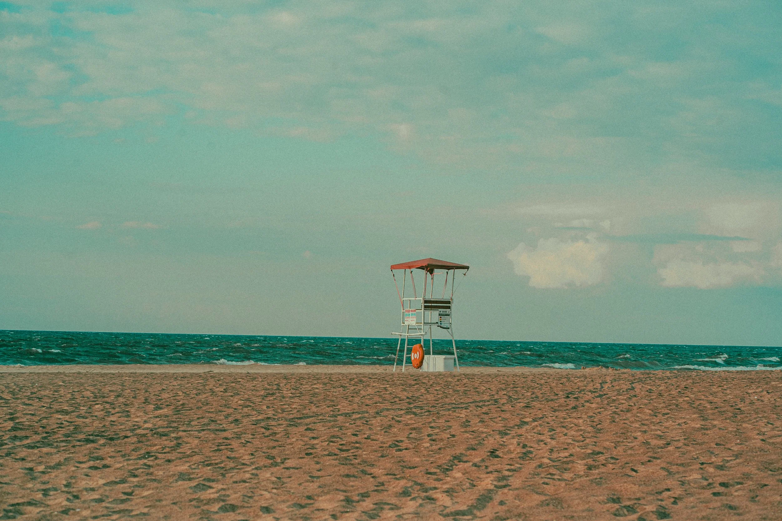 Lifeguard tower on a sandy beach near the ocean, under a cloudy sky.