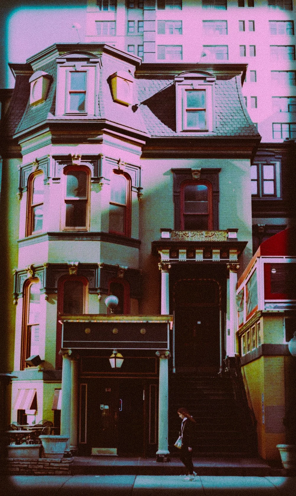 Vintage-style photo of a historic building with ornate architecture and a person walking on the sidewalk.