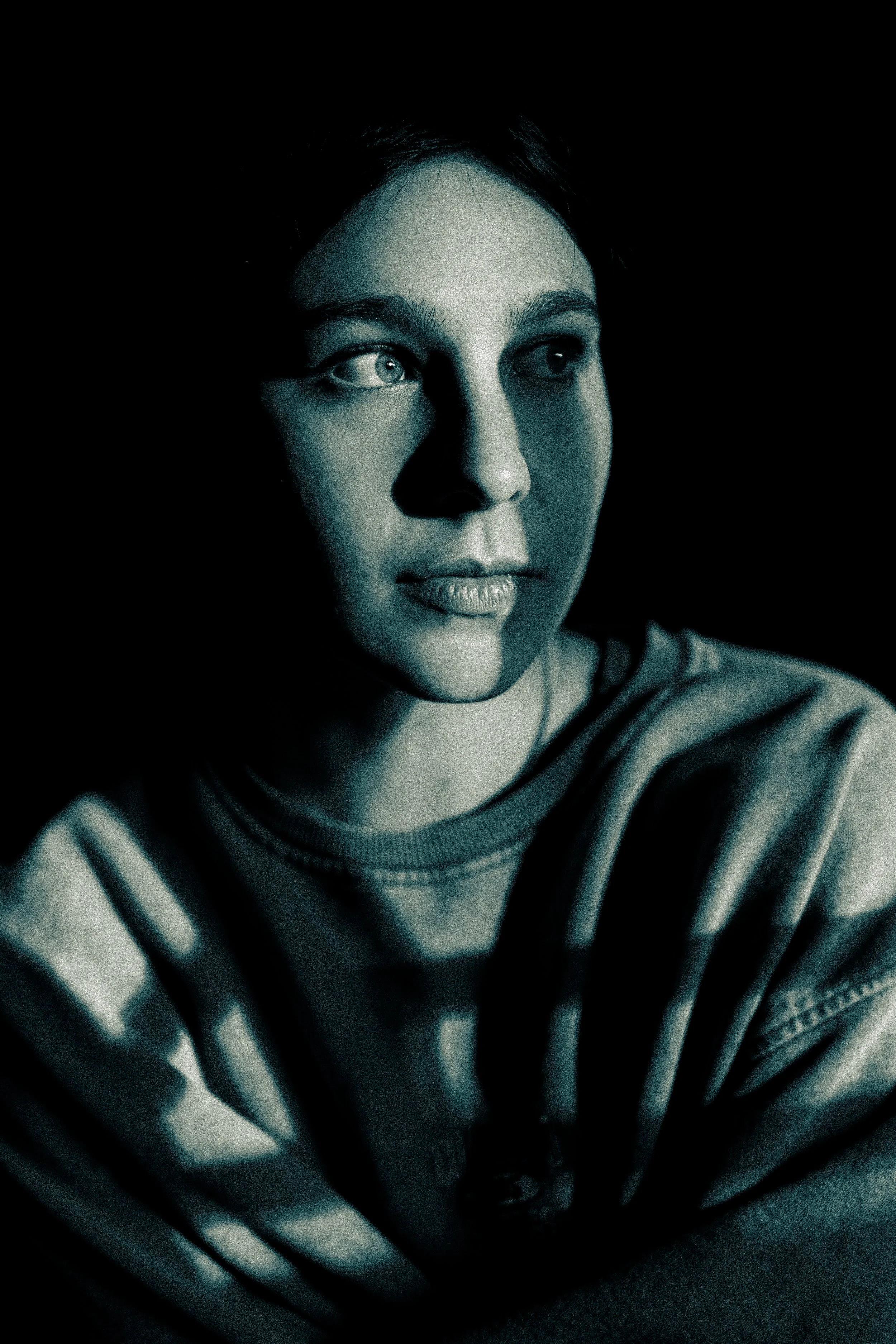 Moody portrait of a person with dramatic shadows, looking to the side, wearing a casual shirt in low lighting.