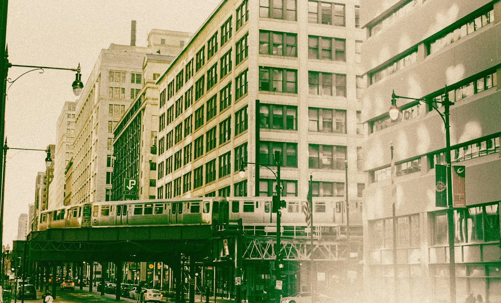 Vintage-style photo of elevated train passing through an urban cityscape with tall buildings and streetlights.