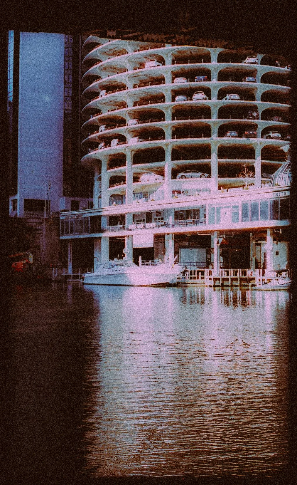Marina City building with round honeycomb structure, cars parked on multiple levels, and water reflection in foreground.