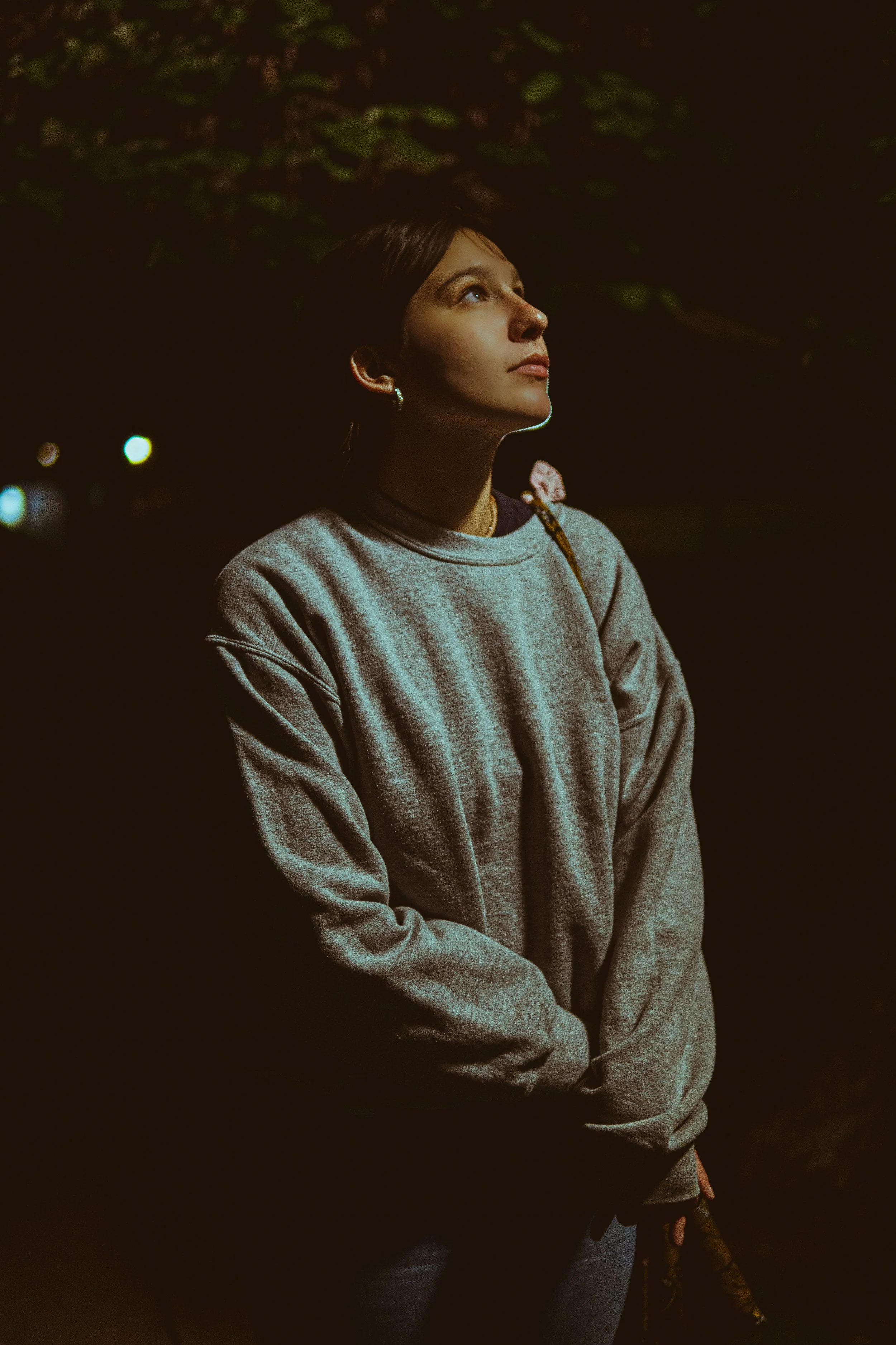Person wearing a gray sweatshirt looking up in a dimly lit outdoor setting.