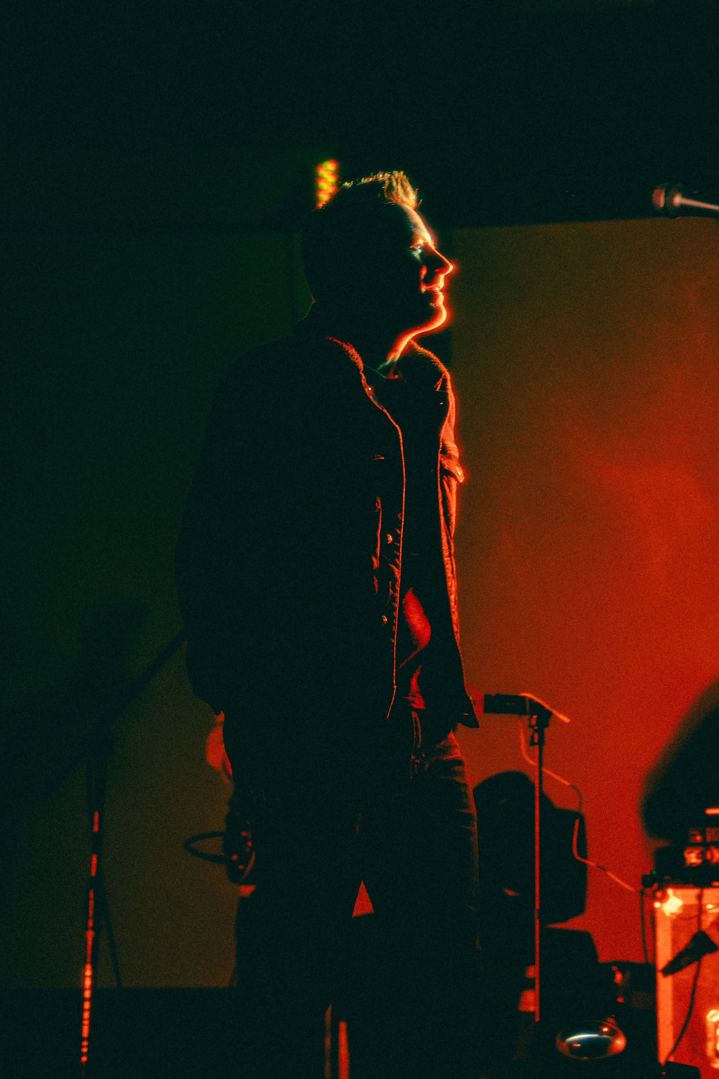 Silhouette of a person with glowing red and orange lighting, standing near a microphone, with musical equipment visible.