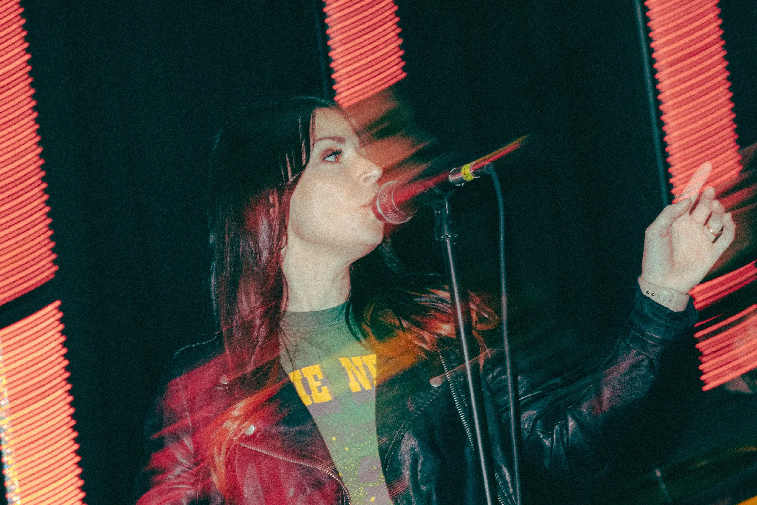 Woman singing into a microphone on stage with motion blur and red light effects.