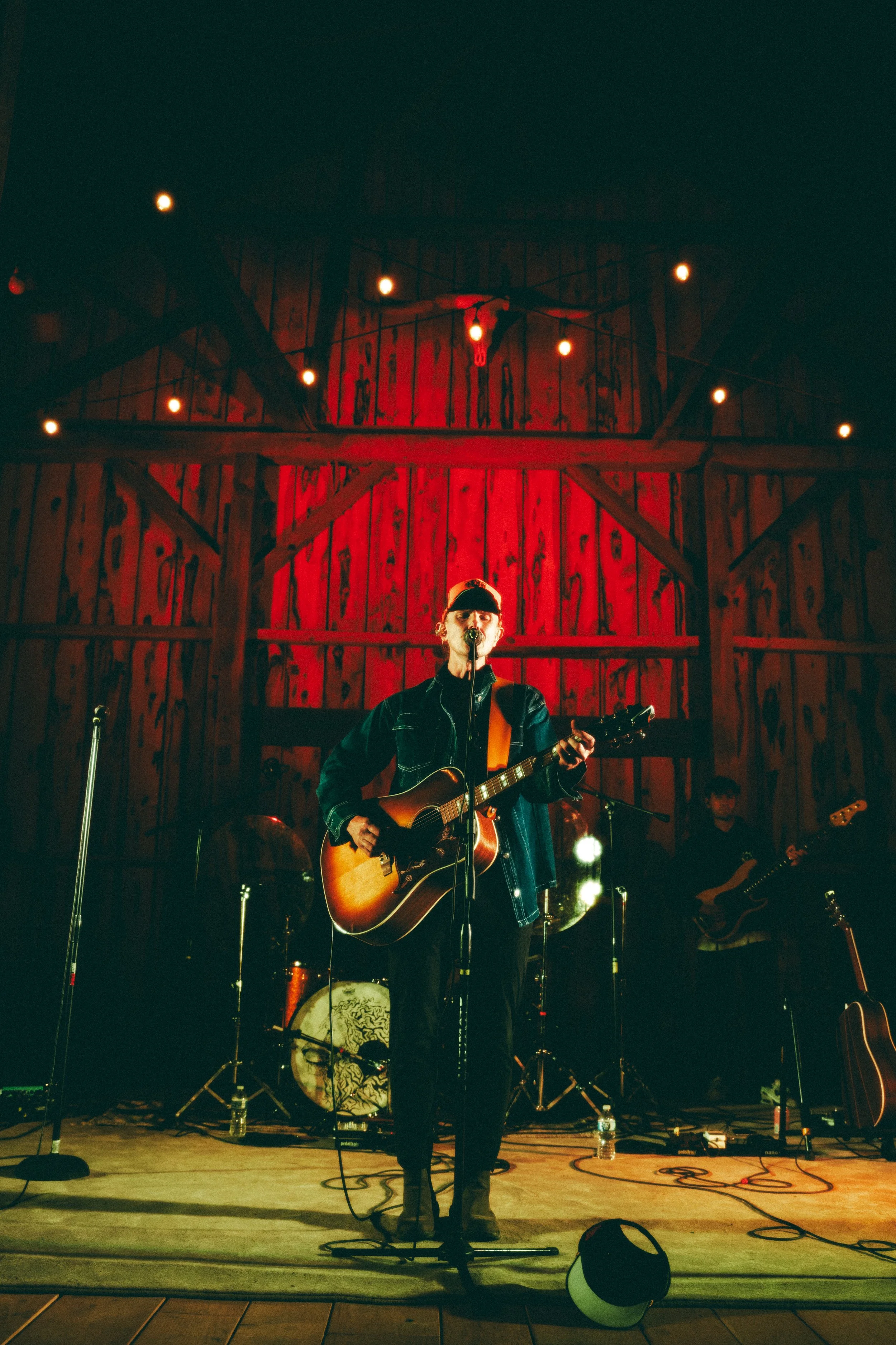 Musician playing acoustic guitar on stage with string lights and wooden backdrop