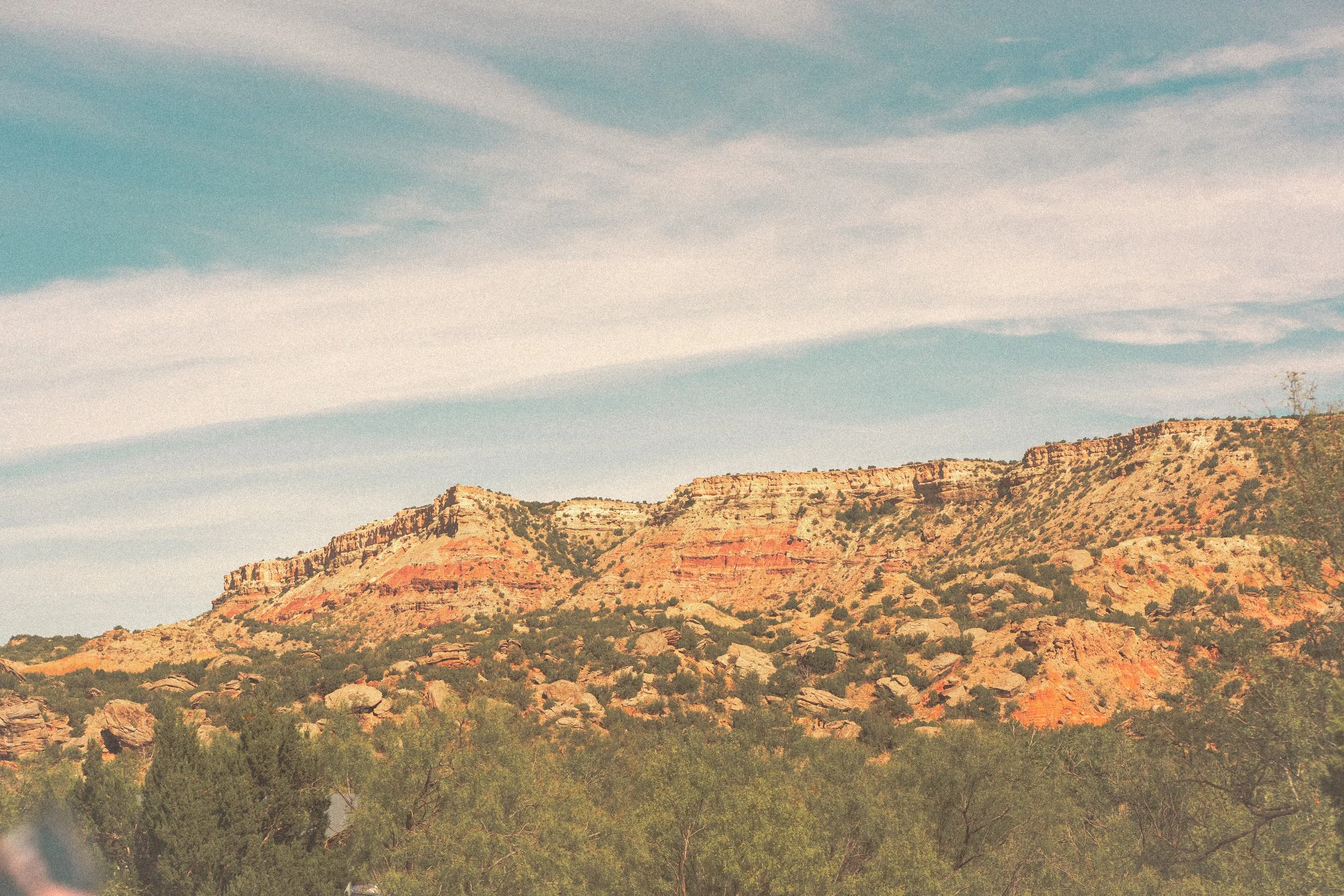 Scenic view of colorful desert cliffs and greenery under a blue sky with clouds.