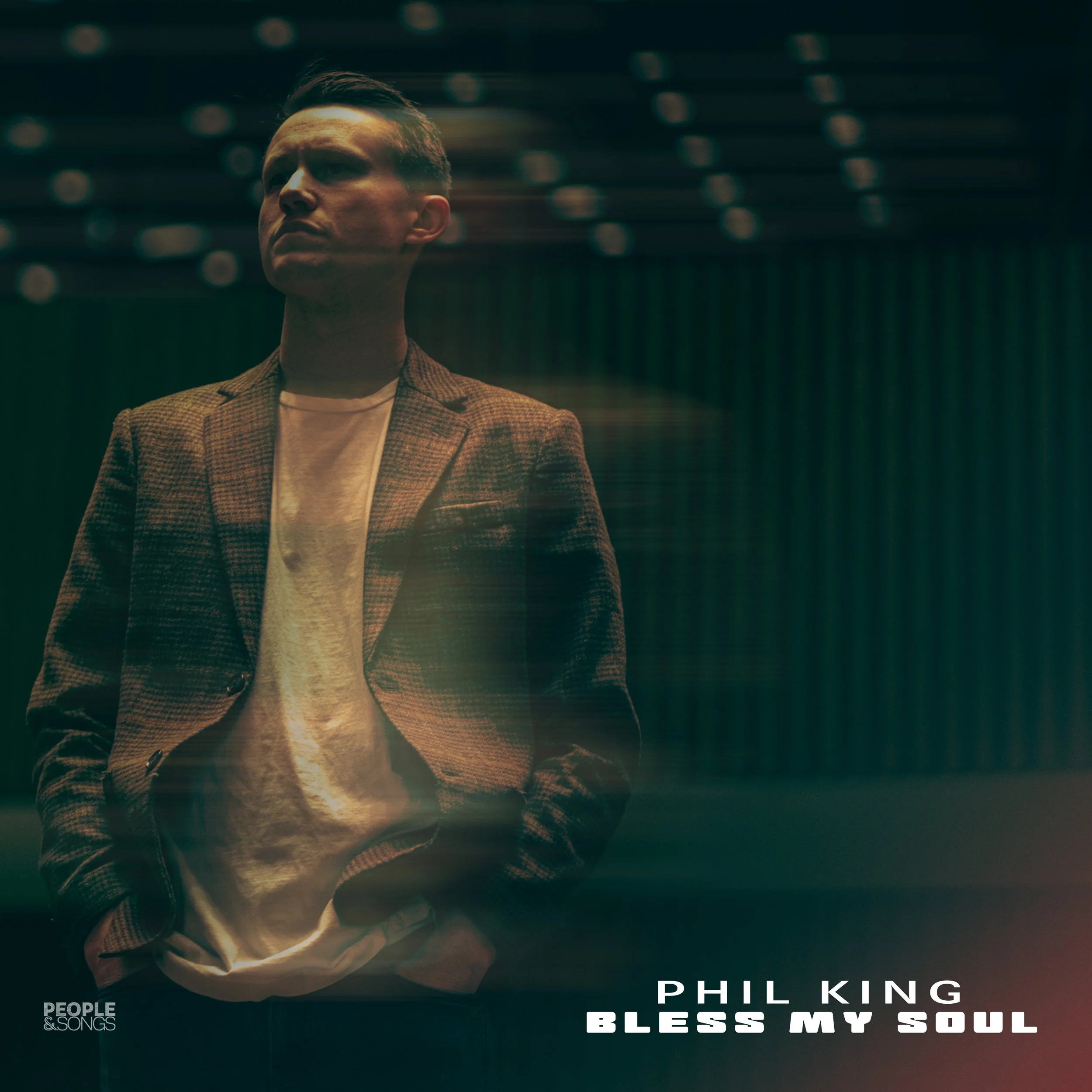 Man in a blazer with a projected overlay, standing in a dimly lit room. Text reads "Phil King, Bless My Soul."