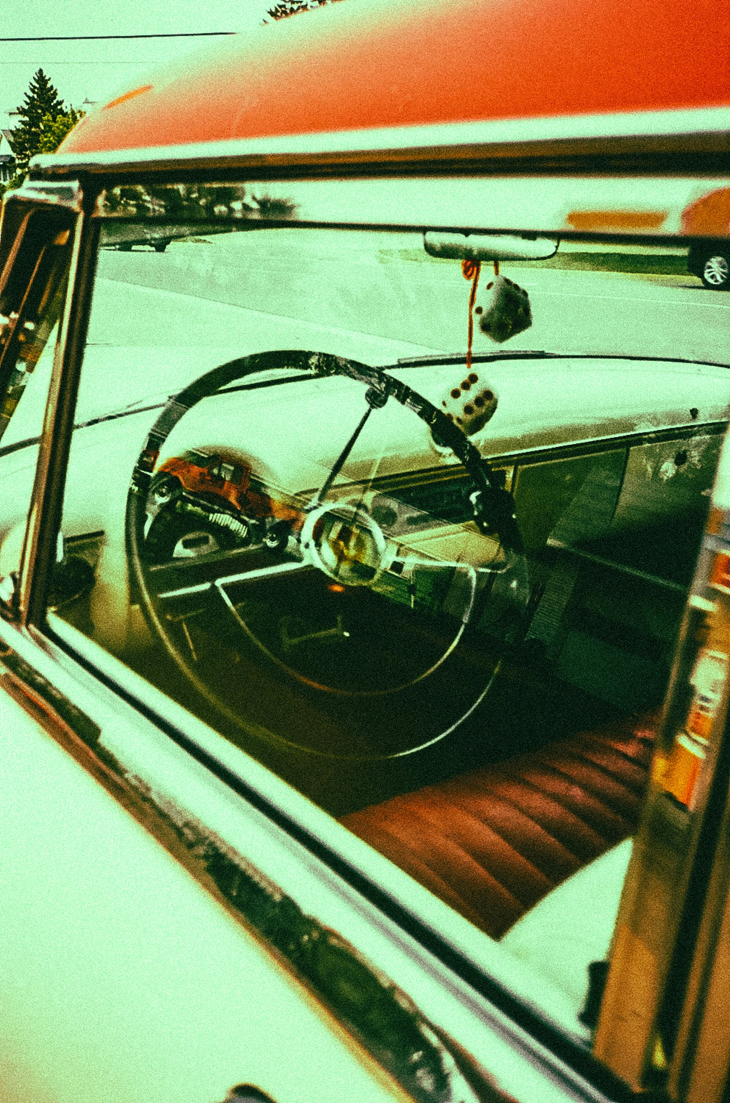 Interior view of a vintage car showing steering wheel and fuzzy dice hanging from the rearview mirror.