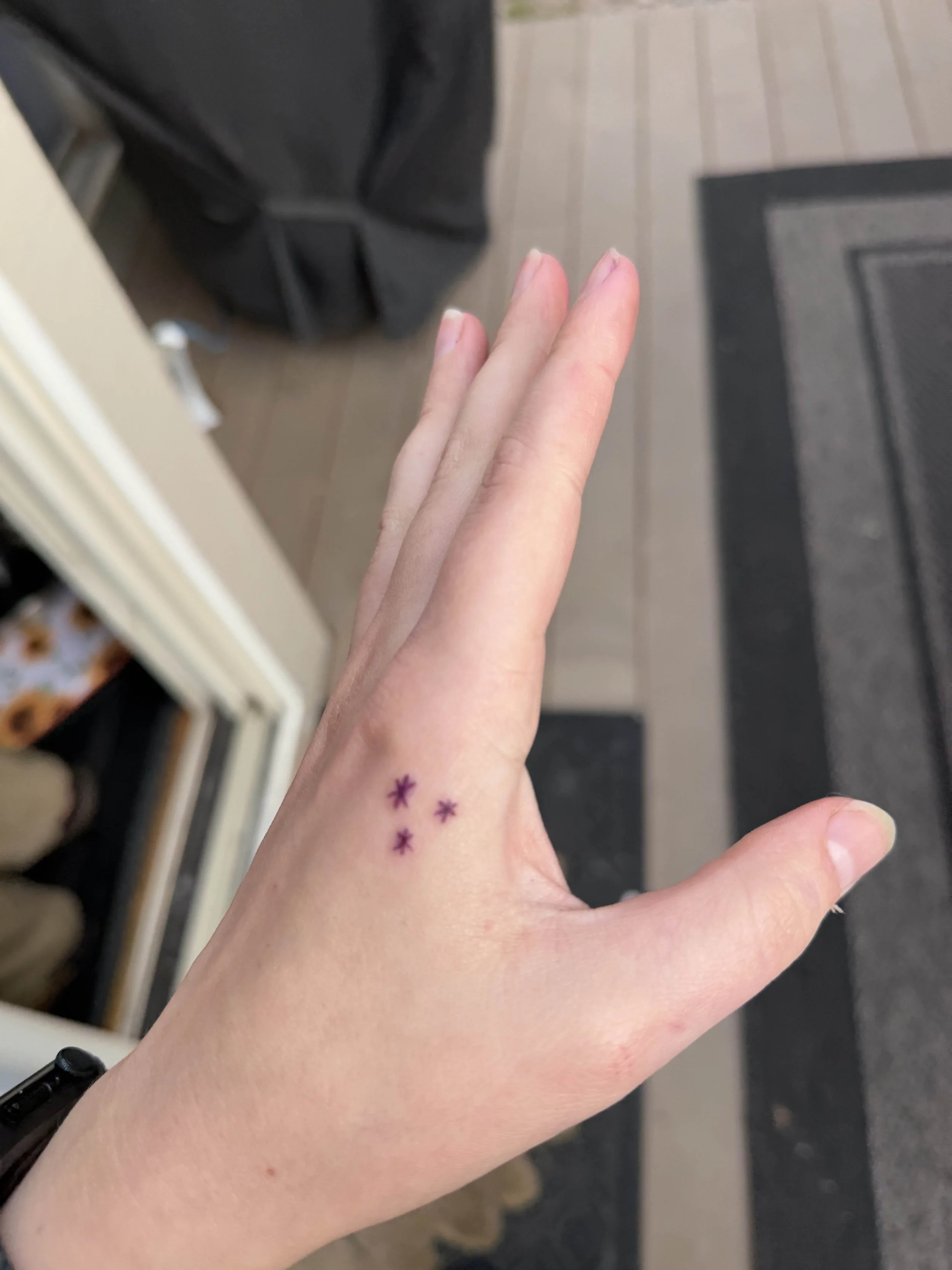 A close-up of a person's hand with three small purple star tattoos on the side near the wrist.