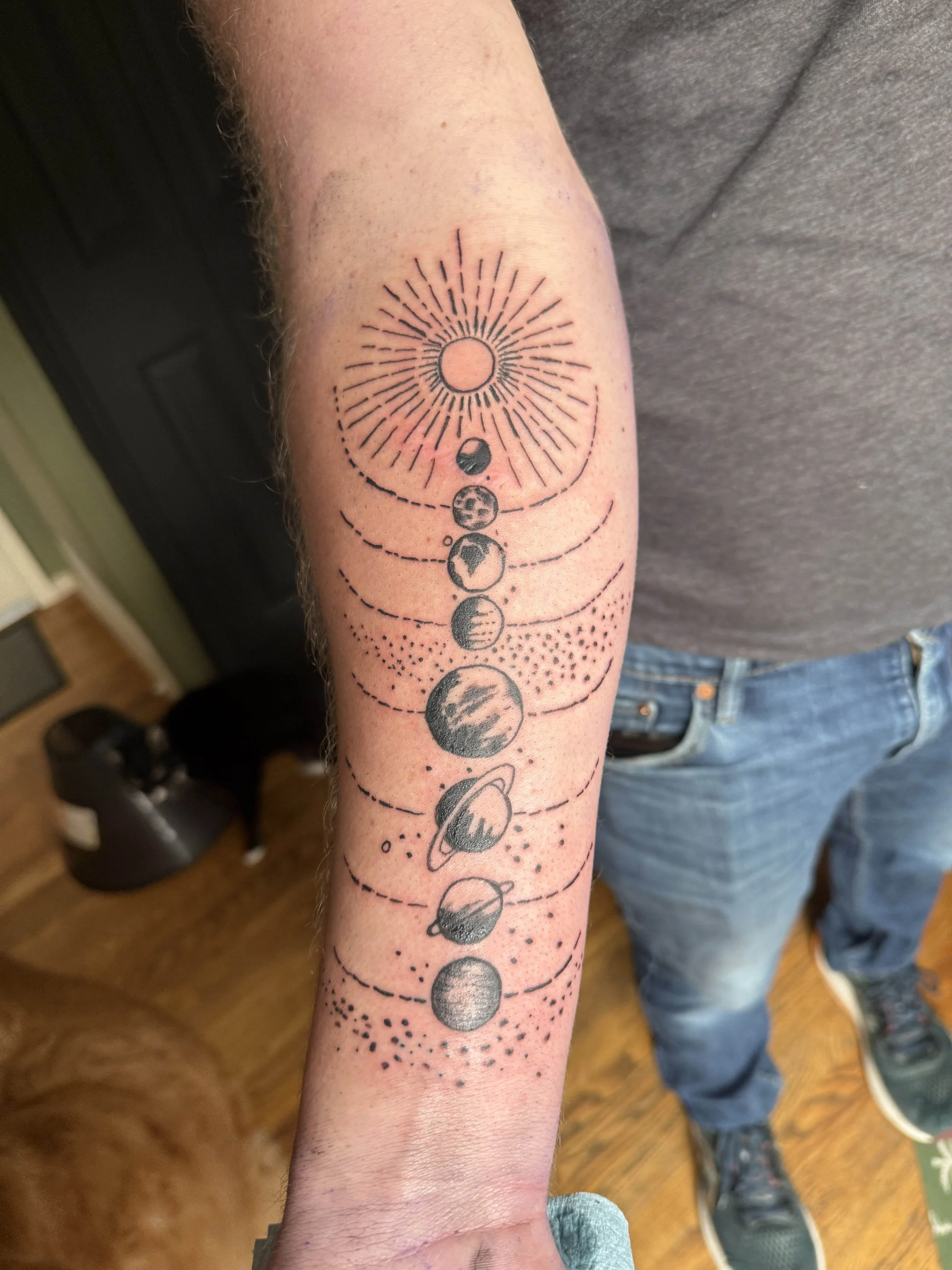 Tattoo of the sun and moon phases with planets and orbital lines on person's forearm.