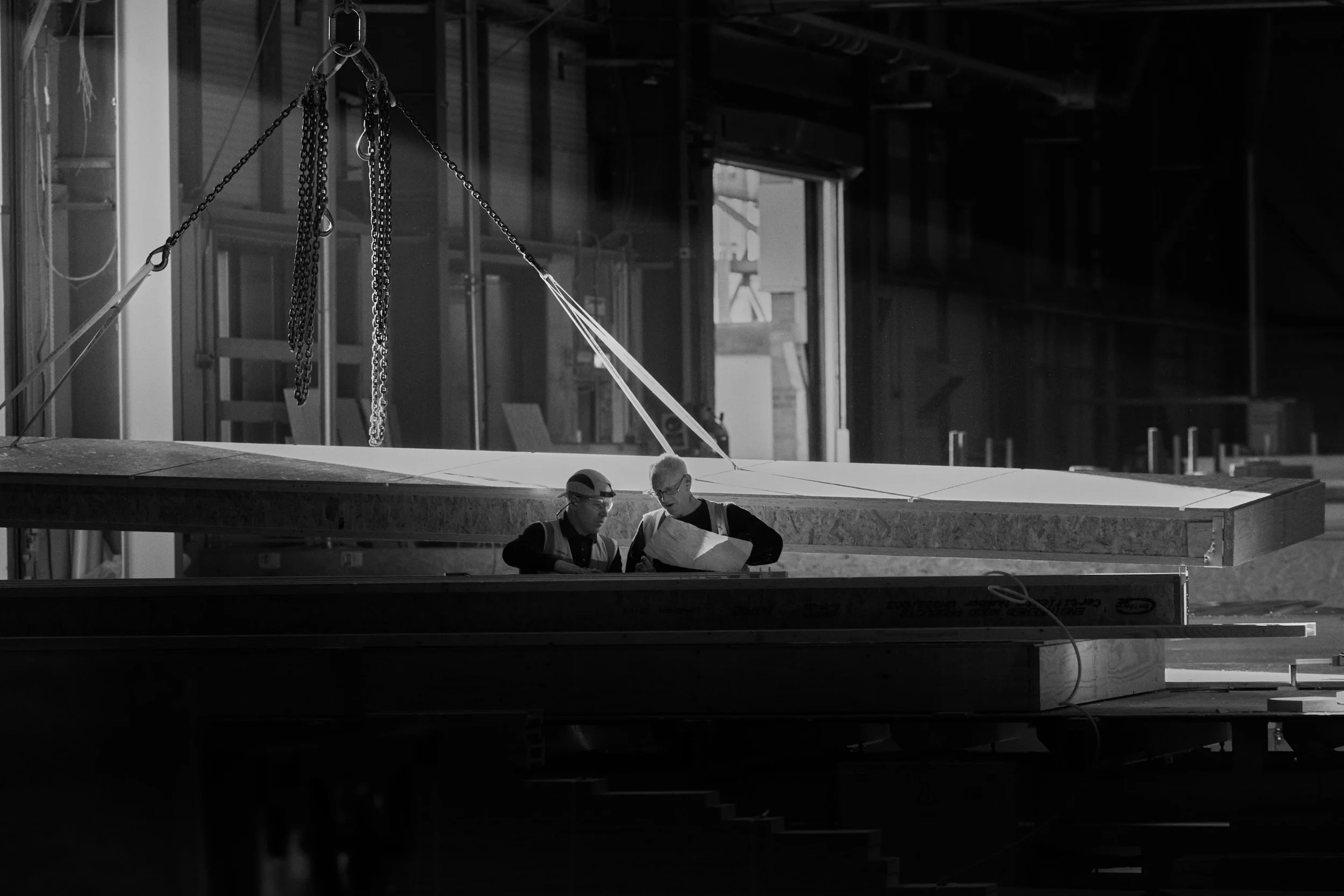 Two construction workers wearing safety glasses and vests reviewing blueprints inside an industrial building under construction.