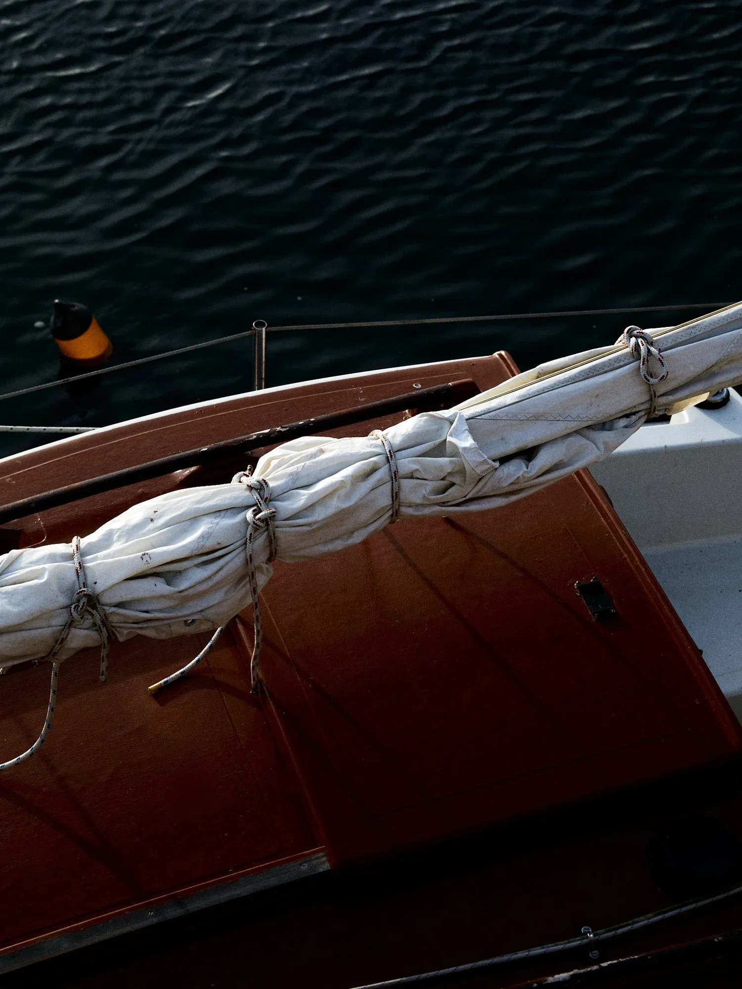 Close-up of a boat with folded sail on deck, dark water in background.
