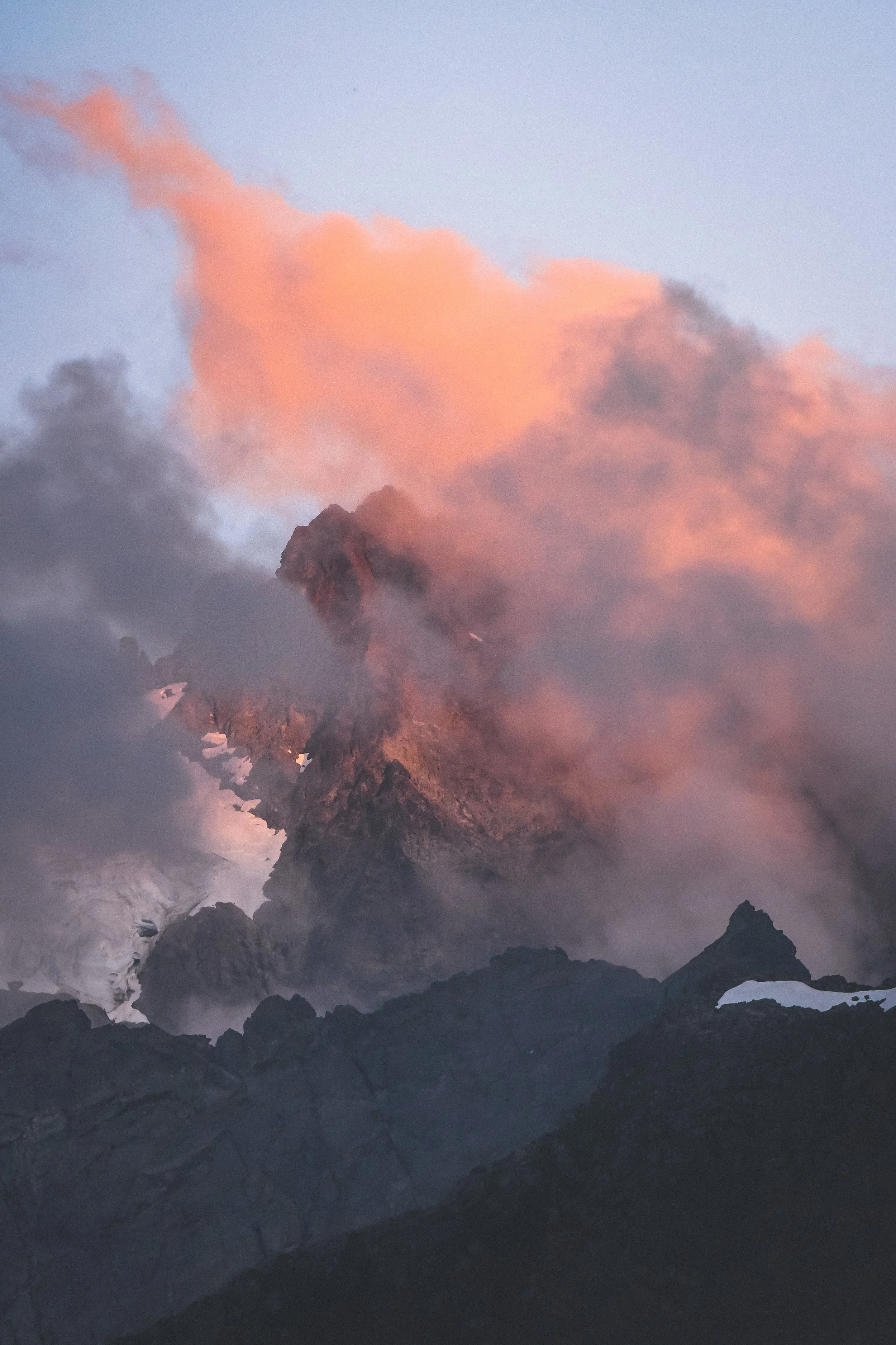 A mountain peak in Washington surrounded by clouds and pinkish-orange sunset light.