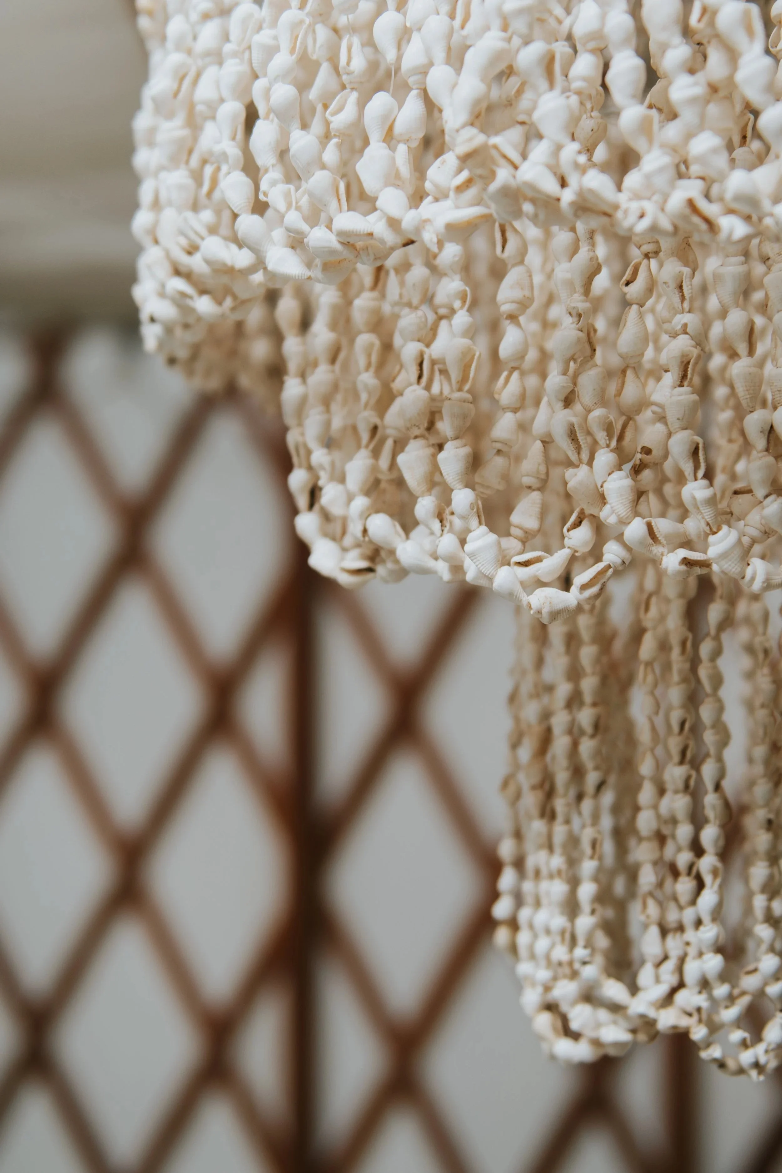 Close-up of a decorative white shell curtain hanging on a metal chain-link fence.