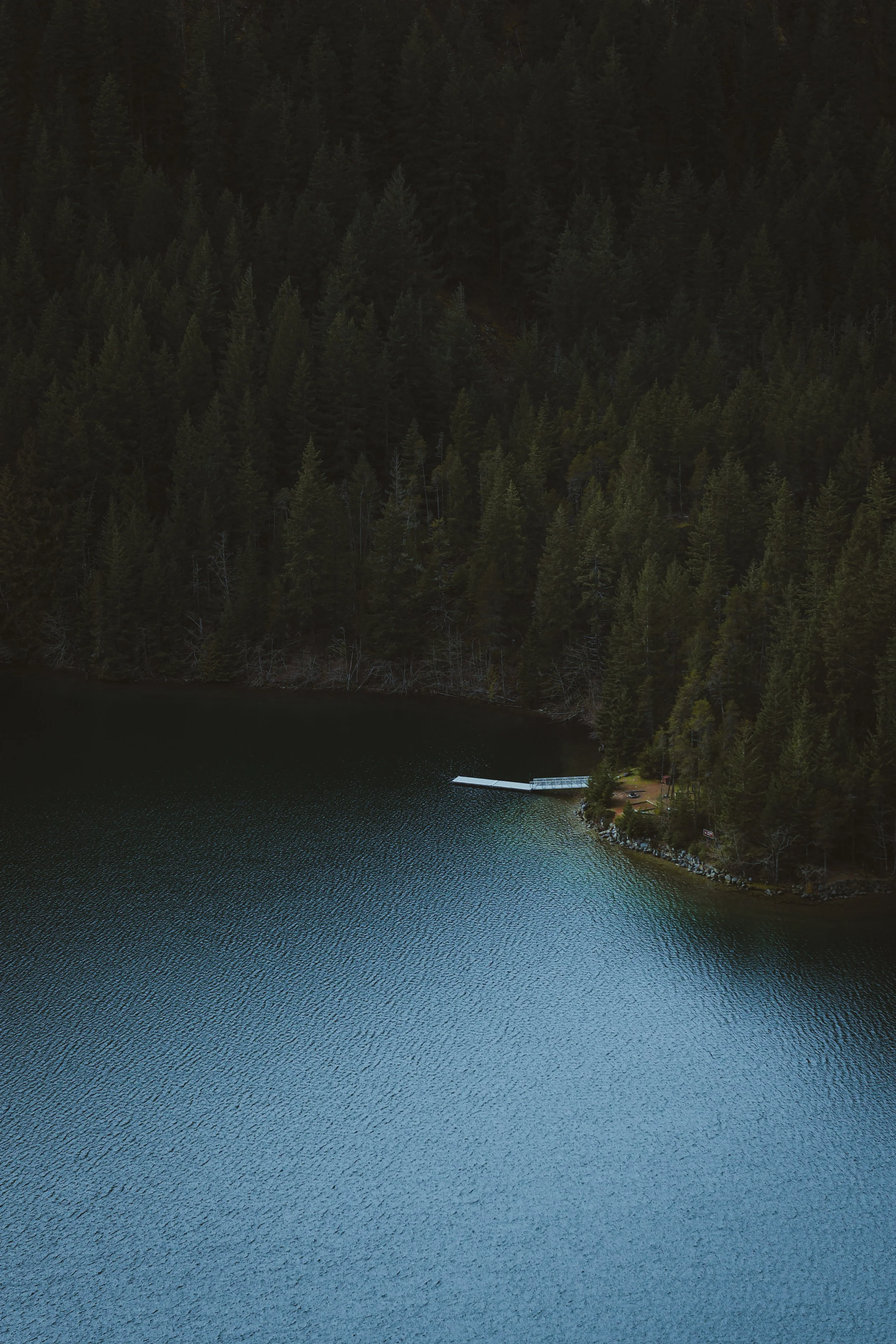 Aerial view of a lake in the North Cascades surrounded by dense forest with calm water and a small dock.