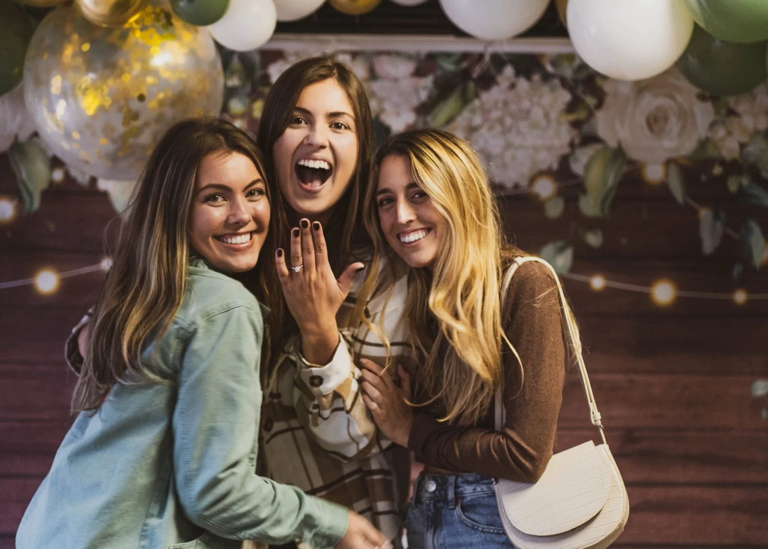 Three women celebrating and smiling at a party with balloons and floral decorations.