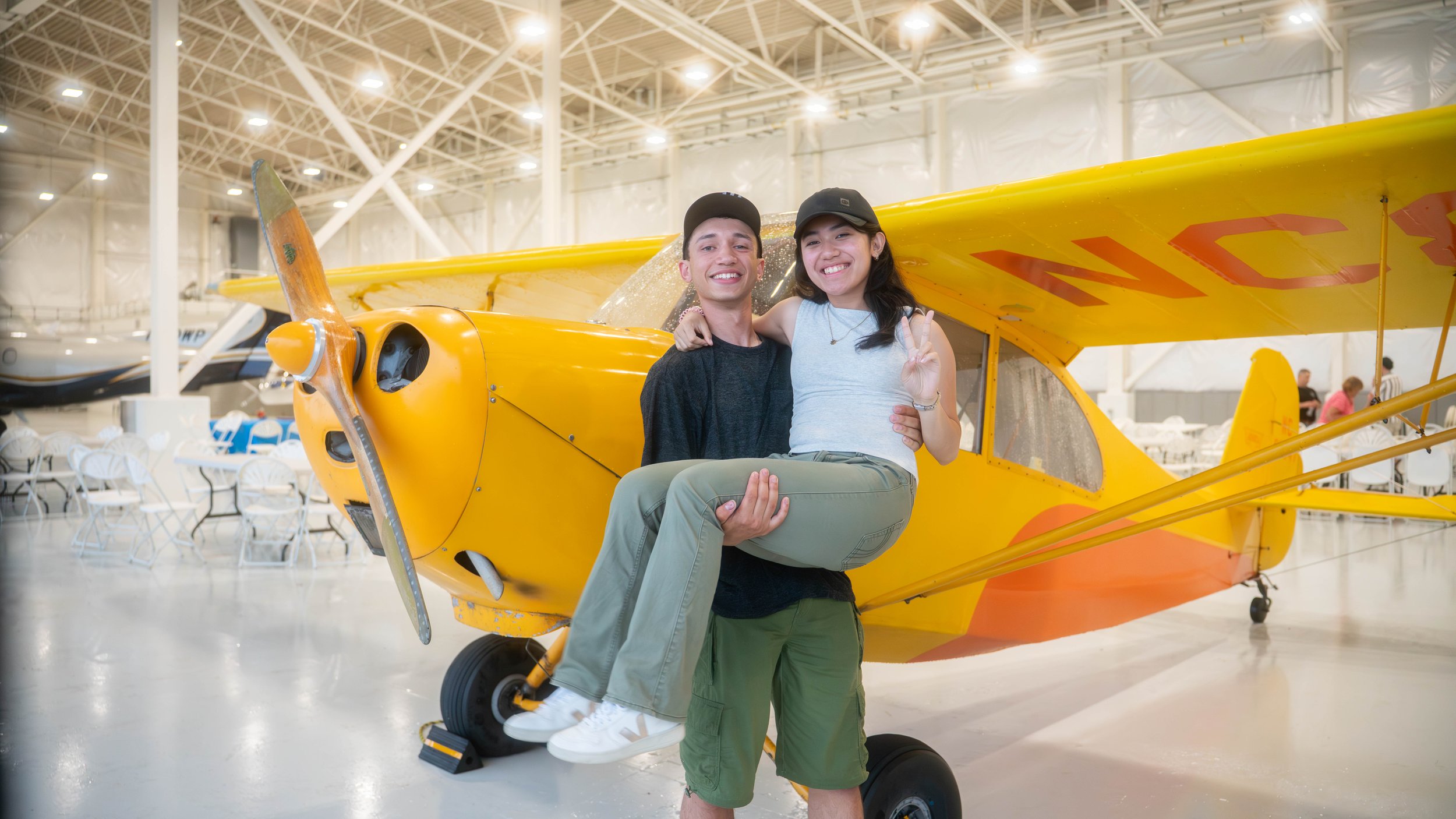 An airplane with a boy holding a girl in front of it.