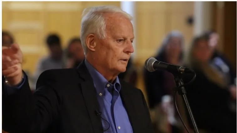 Older man speaking into a microphone during a public event or meeting.