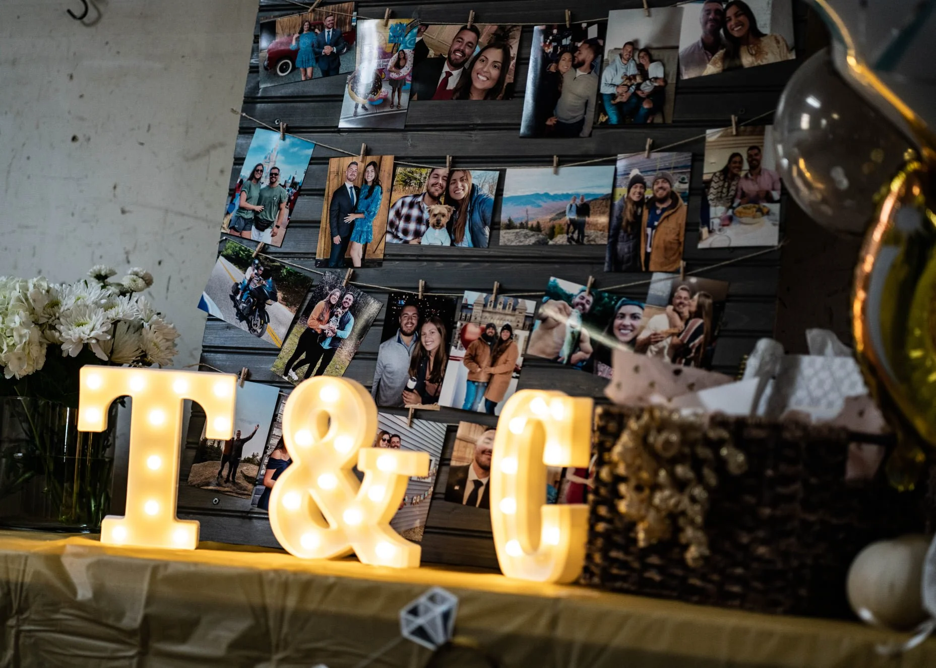 Decorative display of arranged photographs of people, with illuminated marquee letters and a gift box, likely for a celebration or event.