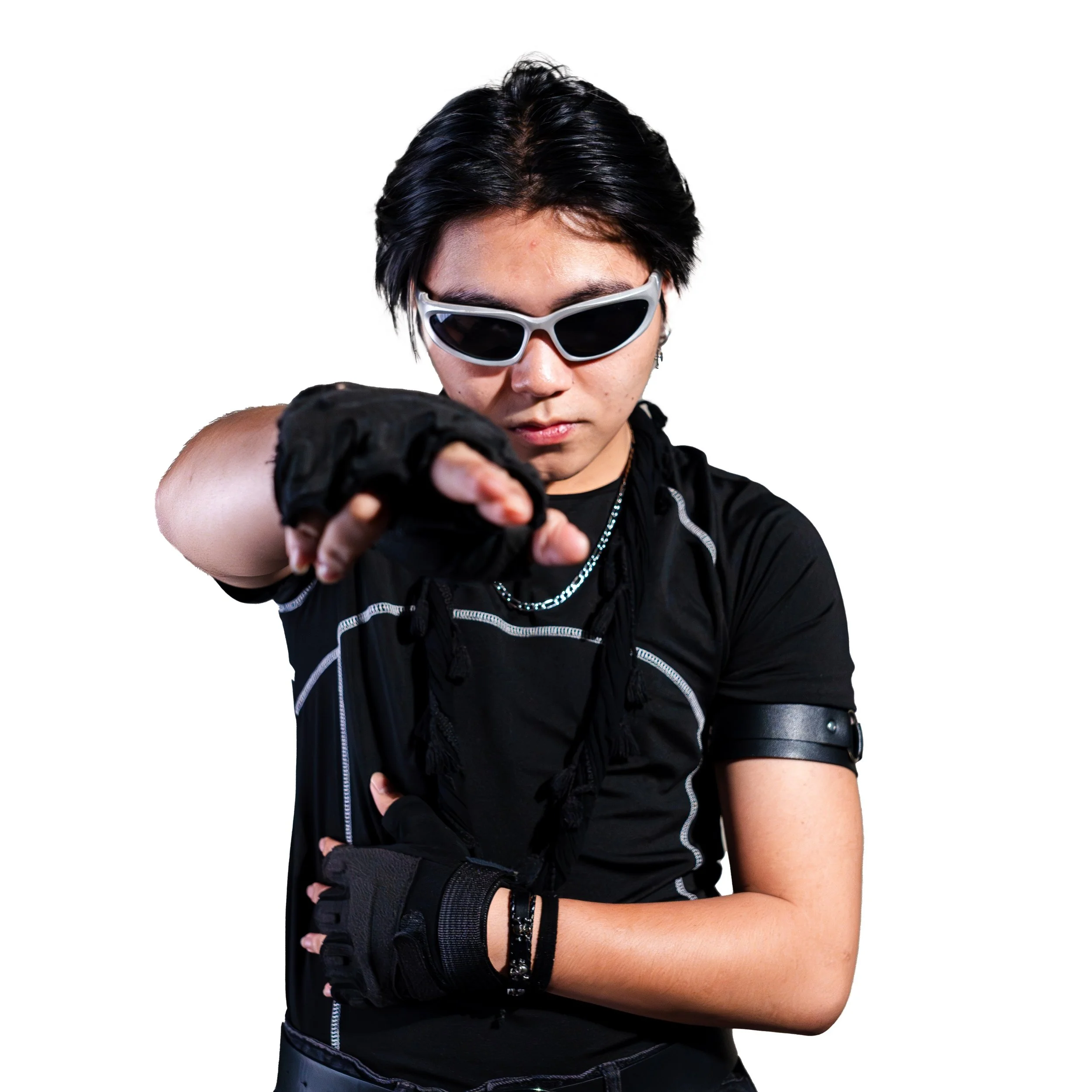 Person with short dark hair wearing white sunglasses, black gloves, black t-shirt, and accessories, pointing forward with a serious expression.