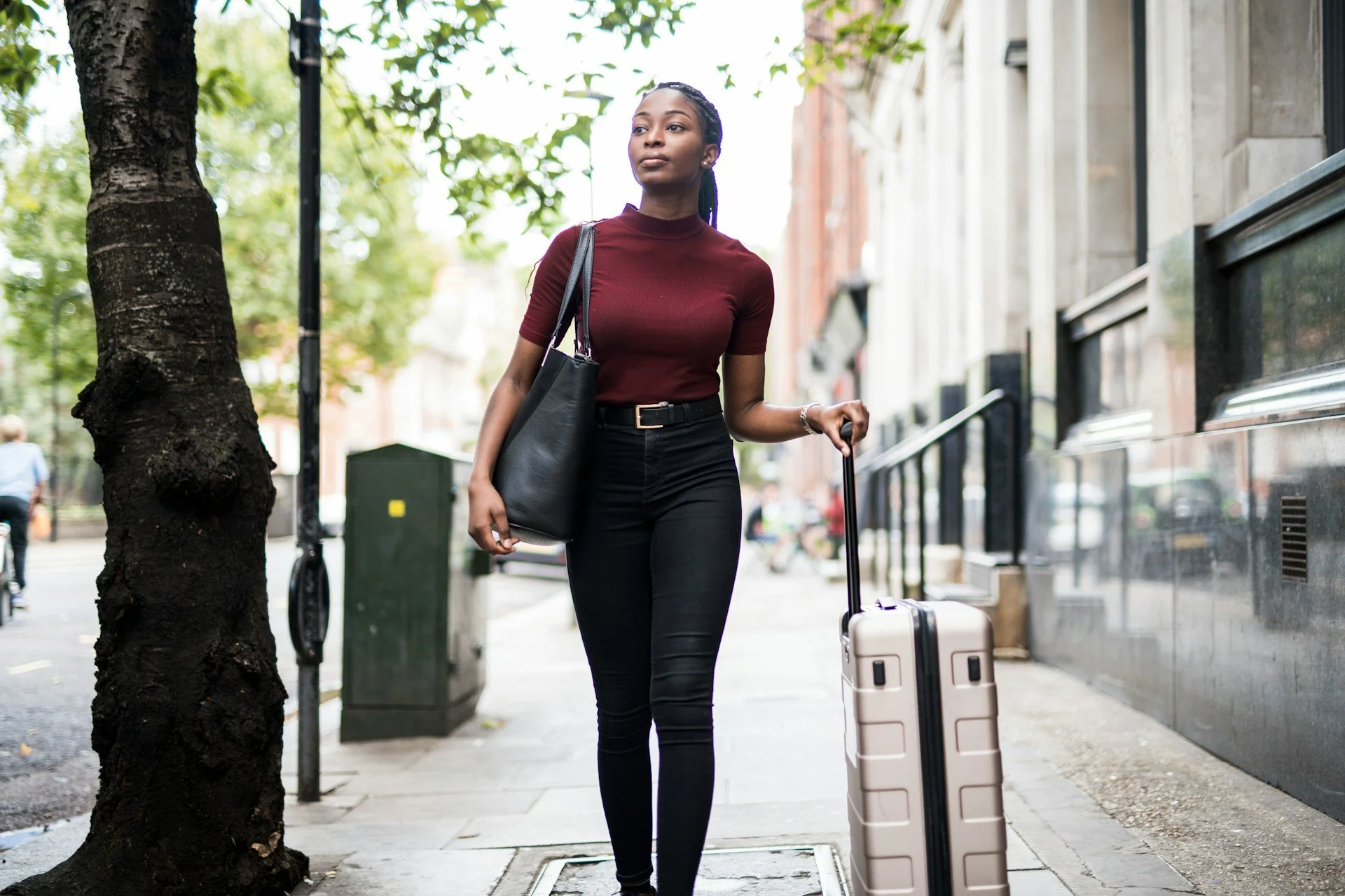 Black professional woman holding a suitcase walking through a city looking determined and reflective