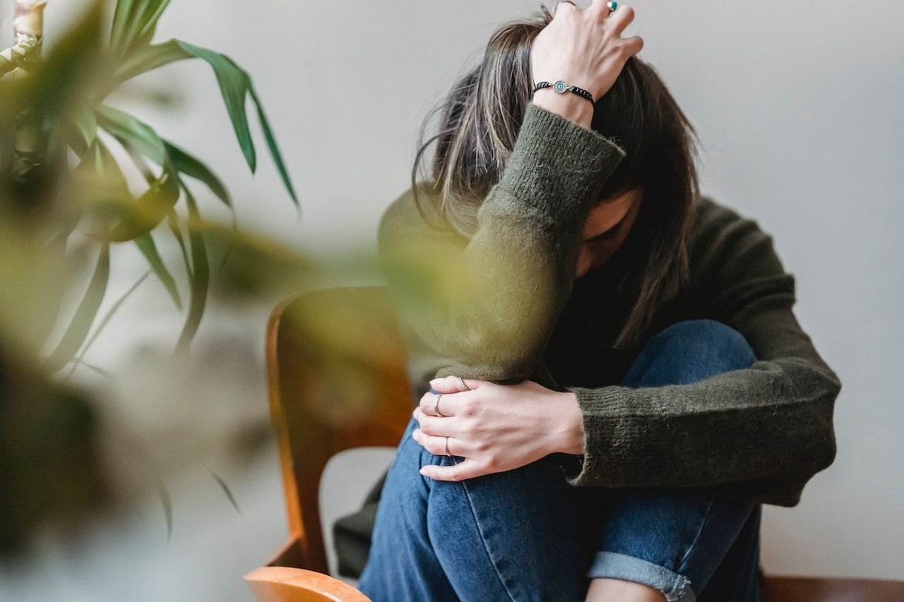 A sad woman in distress sitting on a chair with her hands on her head.