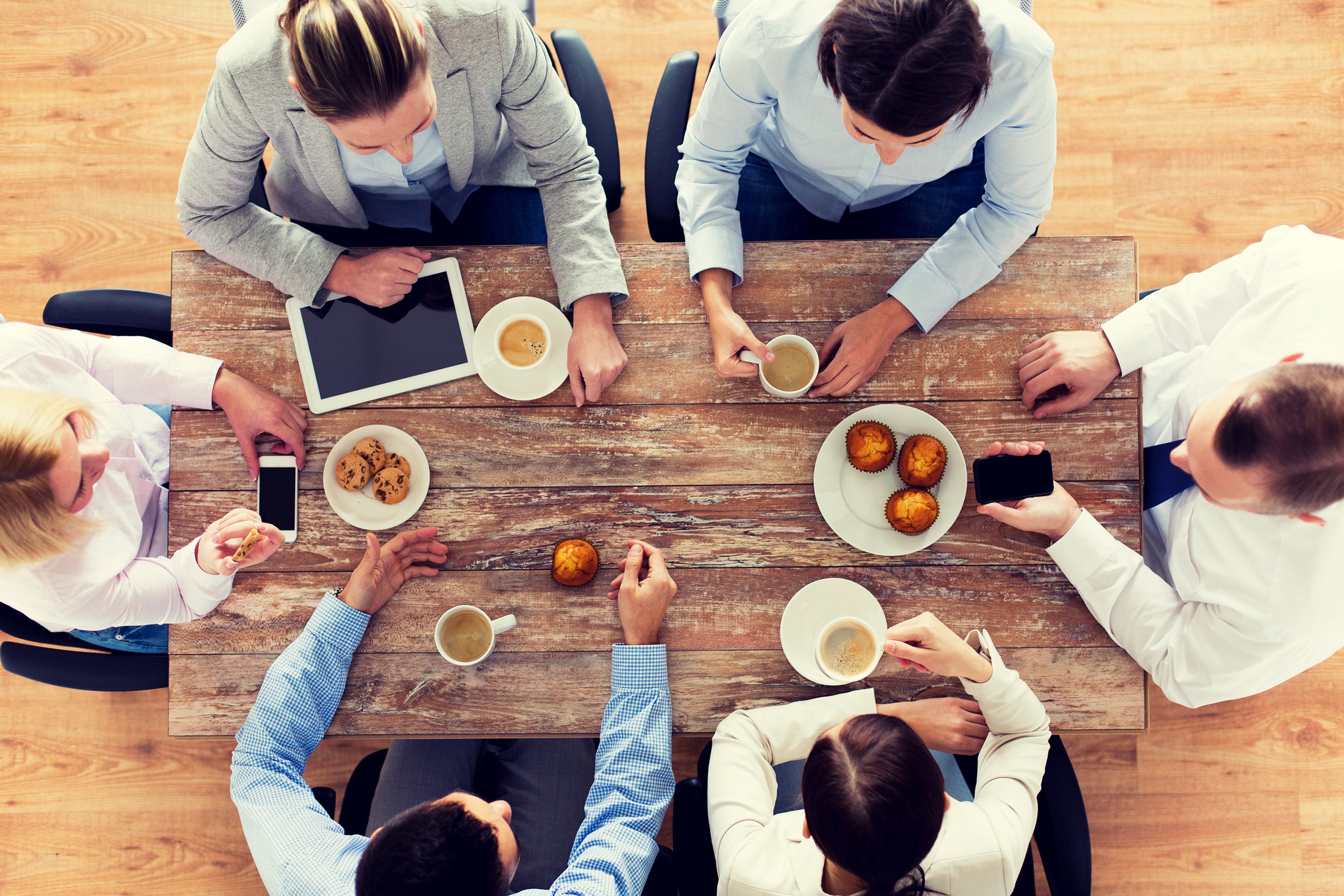 Overhead view of colleagues having a meeting sitting at desk with work laptops, cell phones, coffee, and snacks