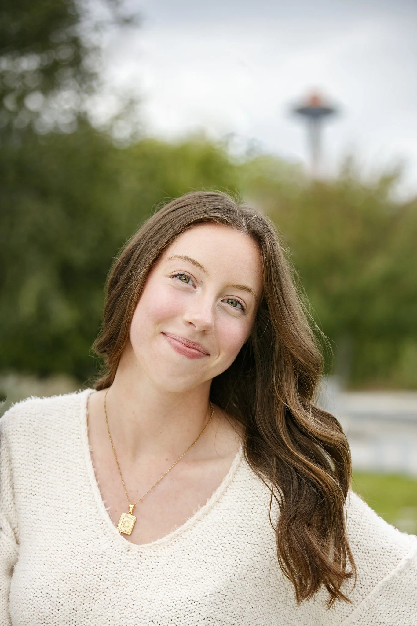 Close up of a young woman smiling in the outdoors against the background of some trees and the Seattle Space Needle