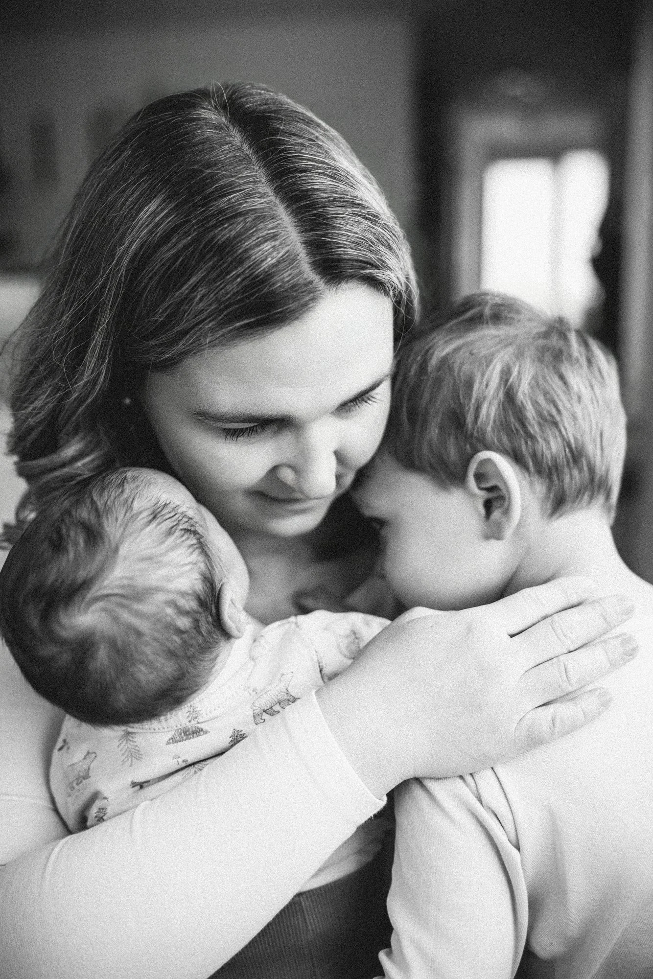 Schwarze und weiße Nahaufnahme einer Mutter, die zwei kleine Kinder liebevoll umarmt.