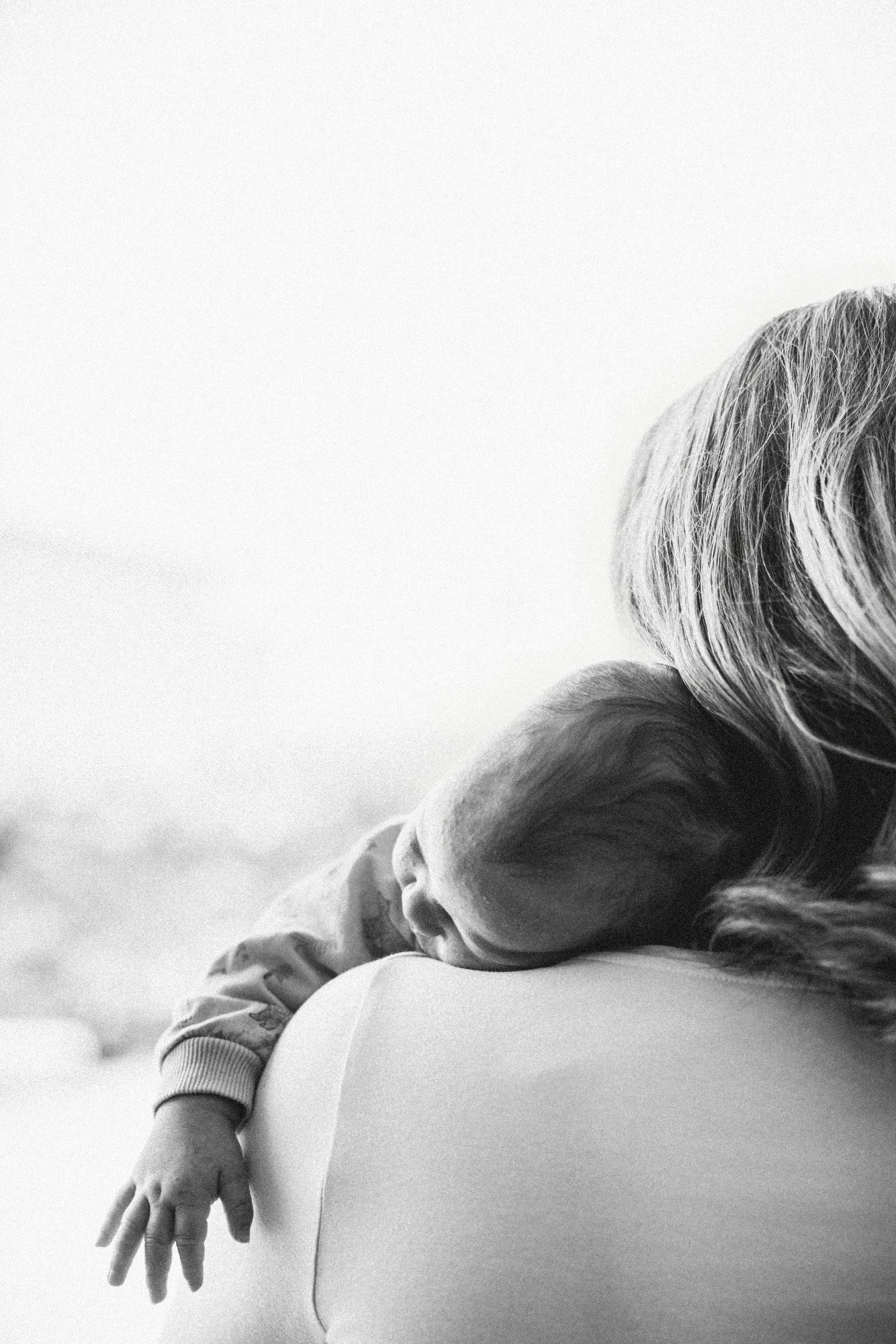 Schwarz-Weiß-Foto einer Person mit einem Baby, das auf der Schulter liegt und schläft.