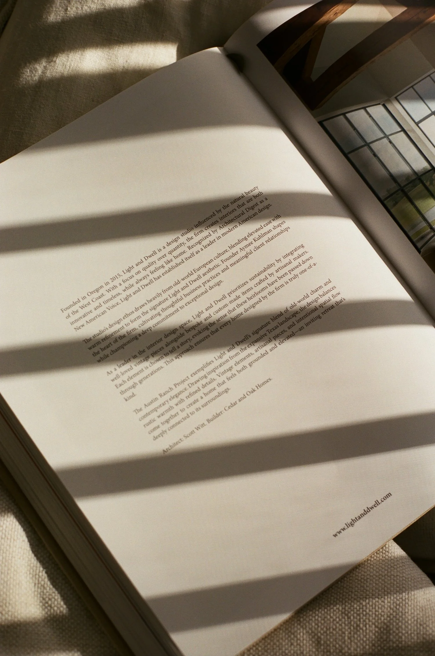 Open book on a desk with sunlight casting shadows on the pages. The text discusses design influence, architecture, and craftsmanship.