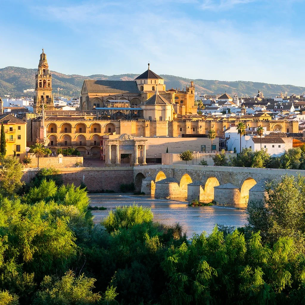 Vista panorámica de la Mezquita-Catedral de Córdoba y el Puente Romano al atardecer, uno de los lugares imprescindibles en una visita desde Sevilla.